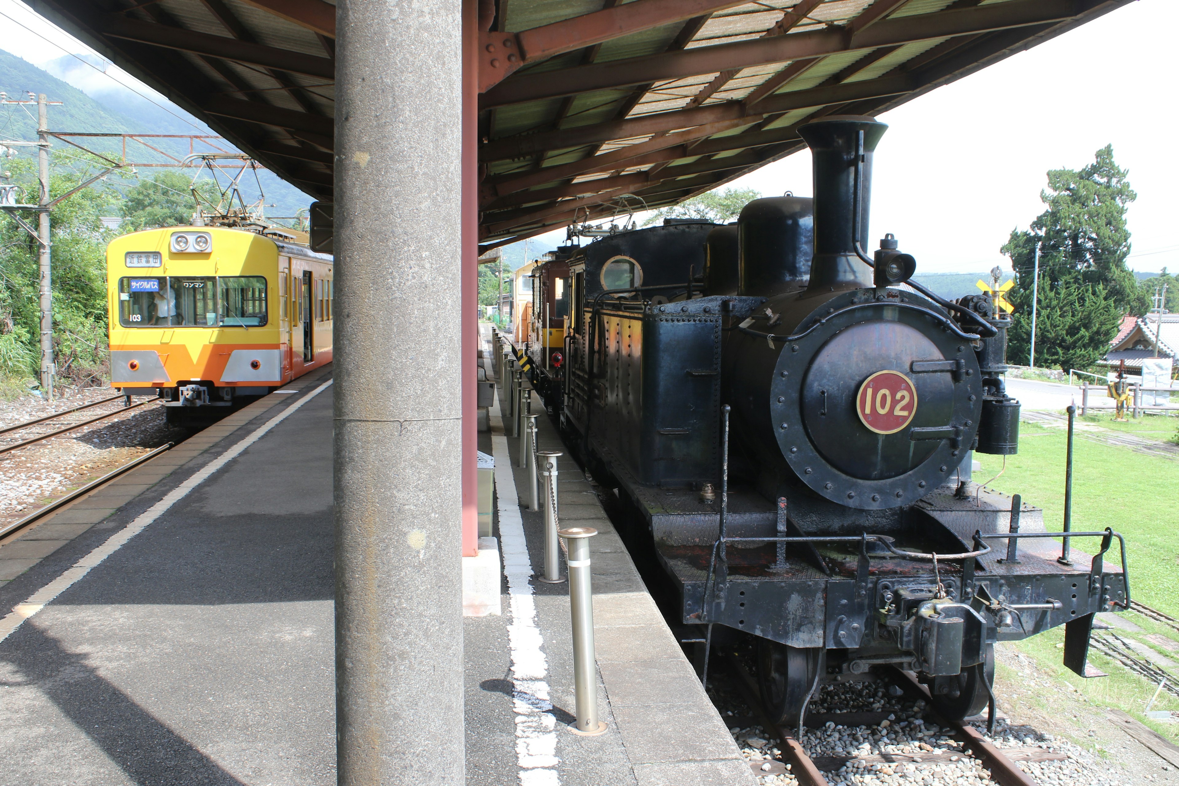 Eine schwarze Dampflokomotive neben einem orangefarbenen Zug an einem Bahnhof