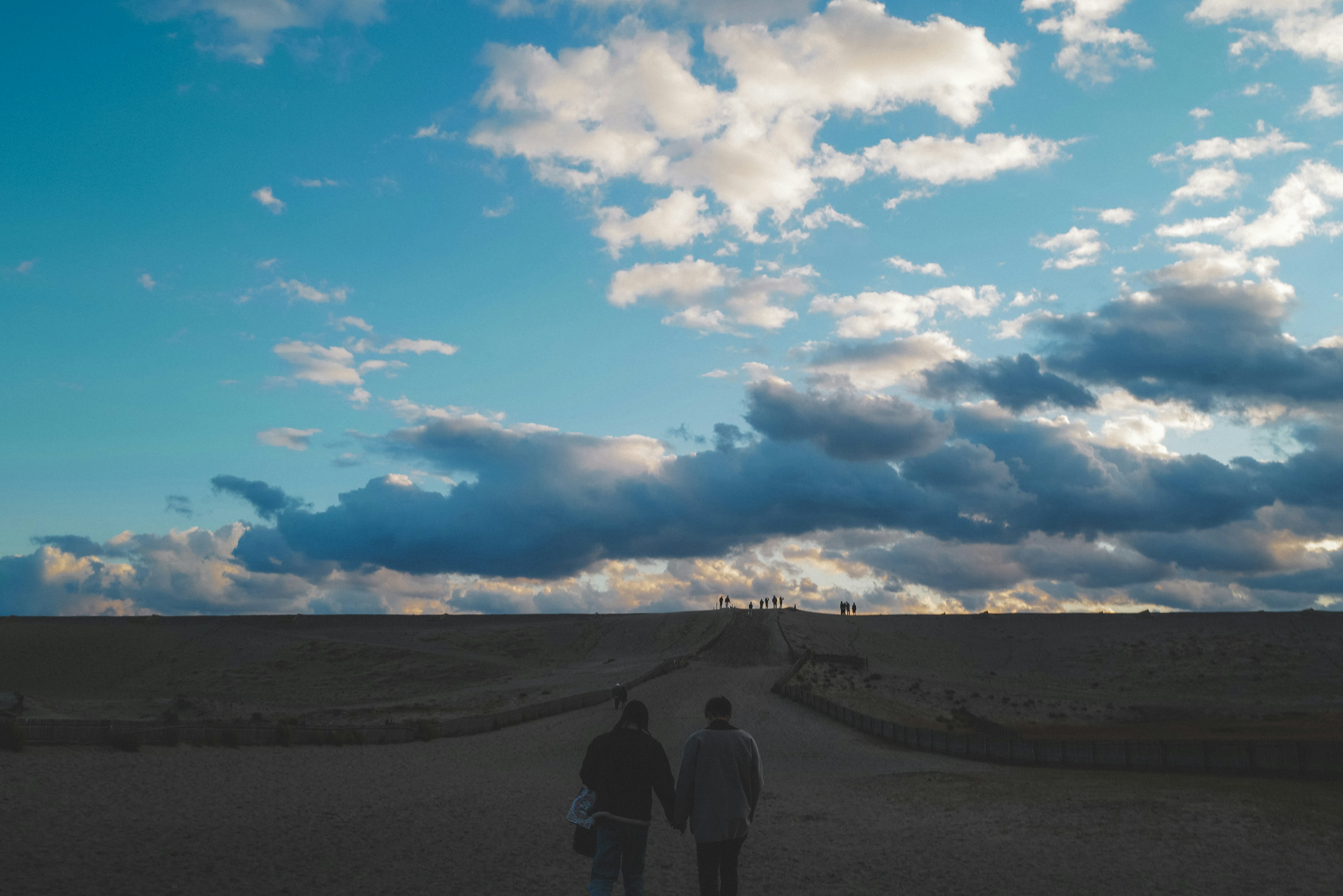 Zwei Personen gehen unter einem blauen Himmel mit Wolken