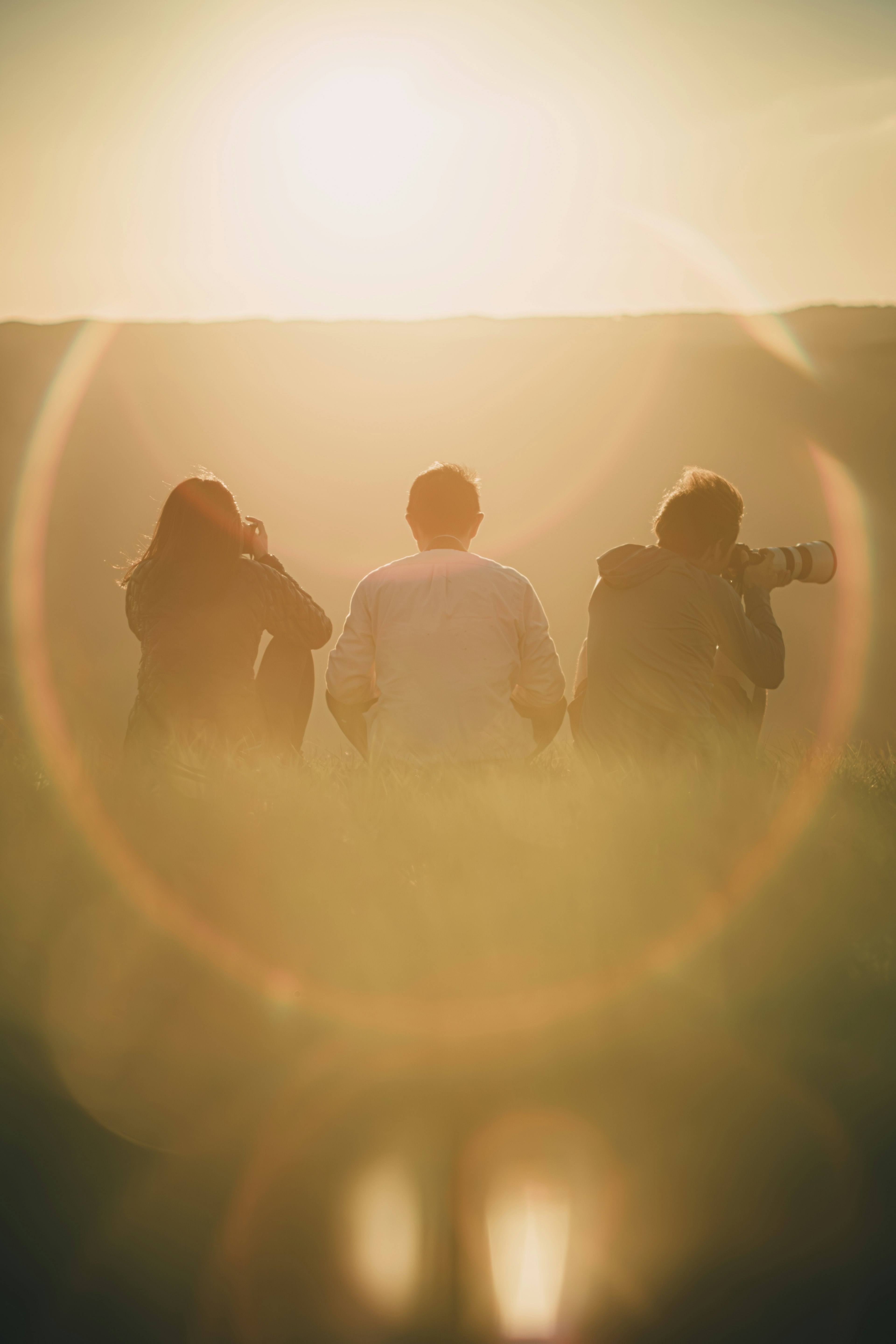 Three figures standing with their backs to the camera against a sunset