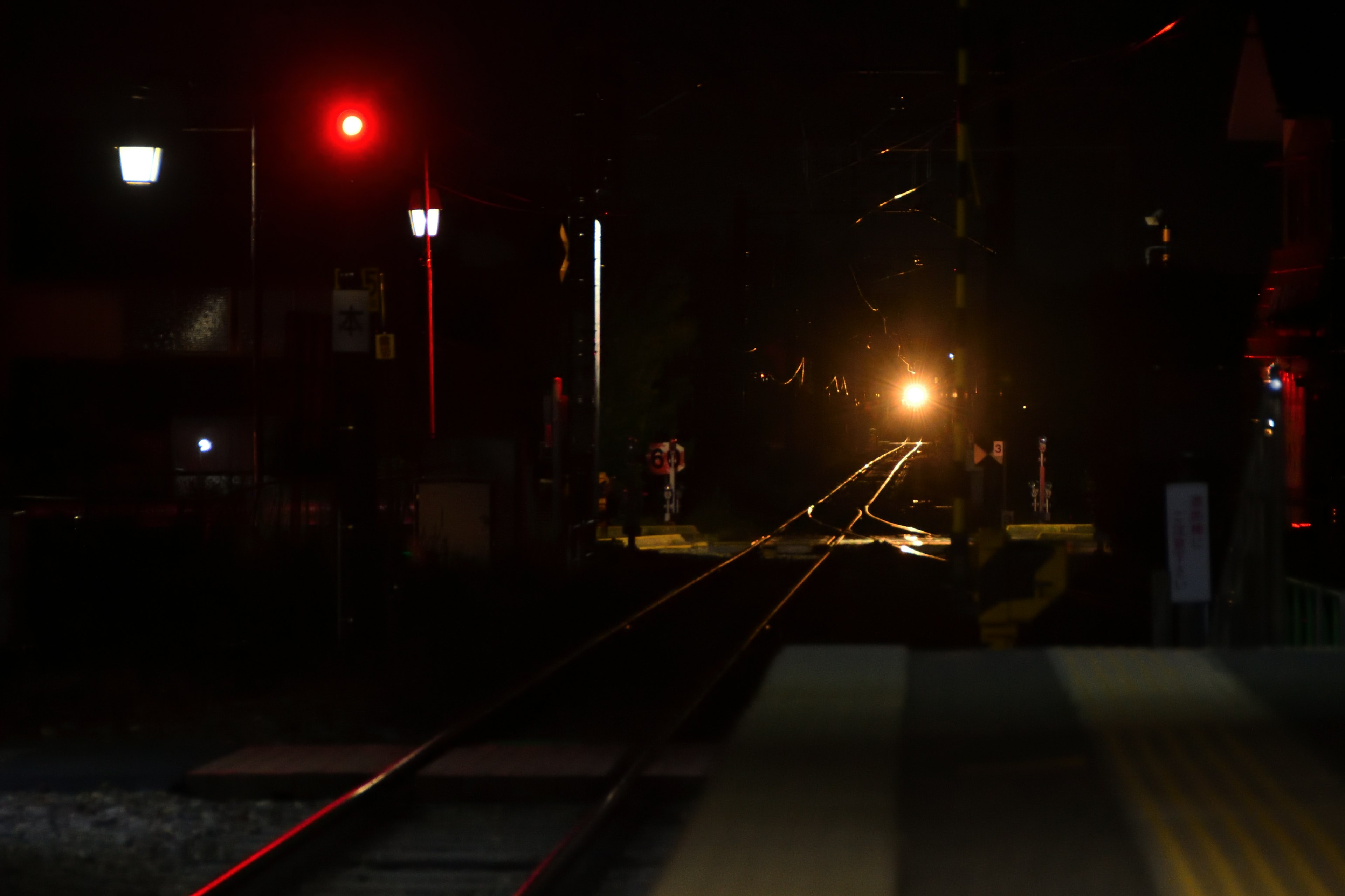 Night scene at a train station with a red signal light and train headlight