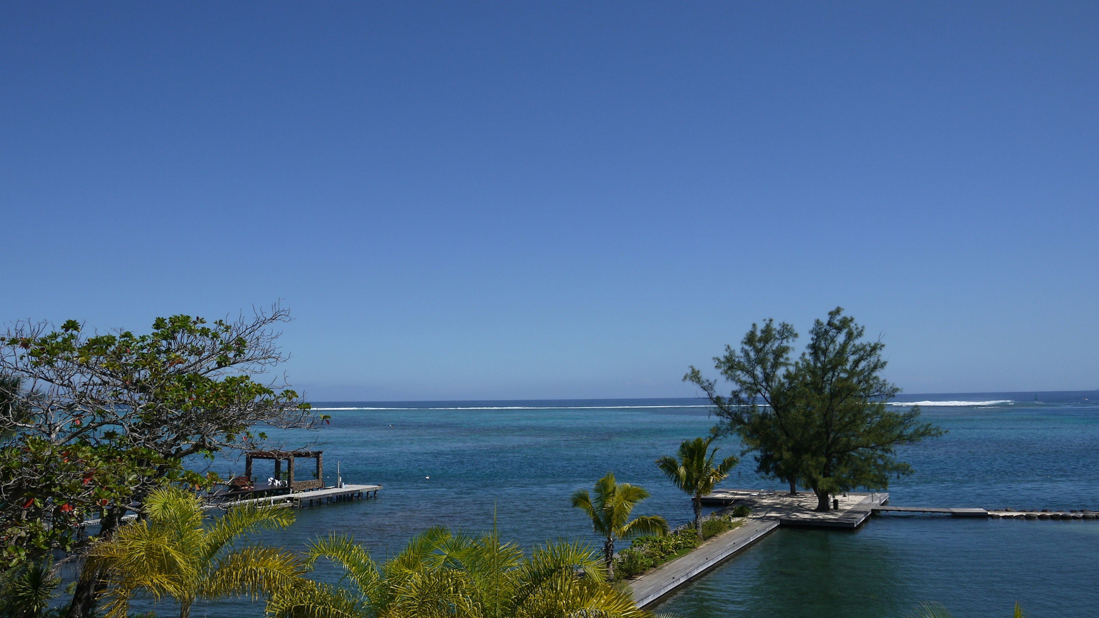 Beautiful landscape with blue ocean and clear sky featuring a pier and trees