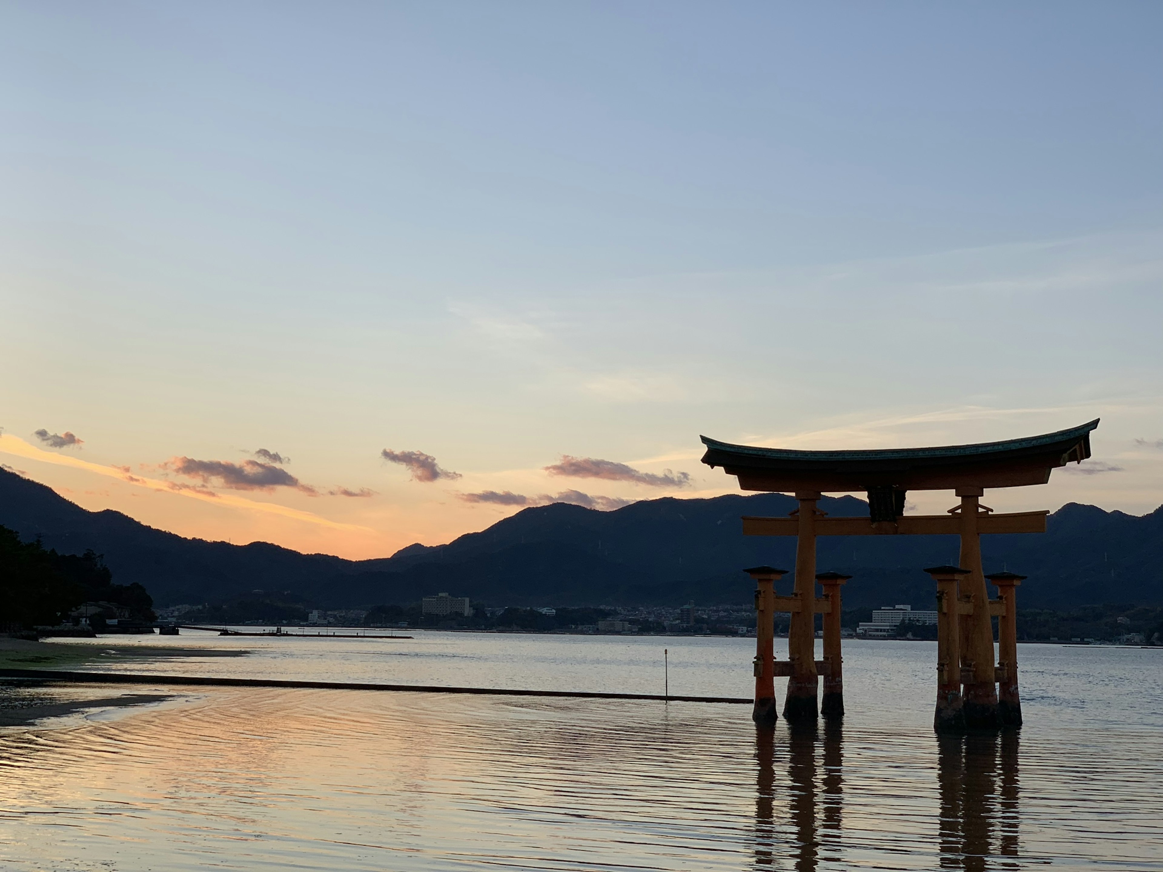 Torii en silueta contra un atardecer sobre aguas tranquilas y montañas