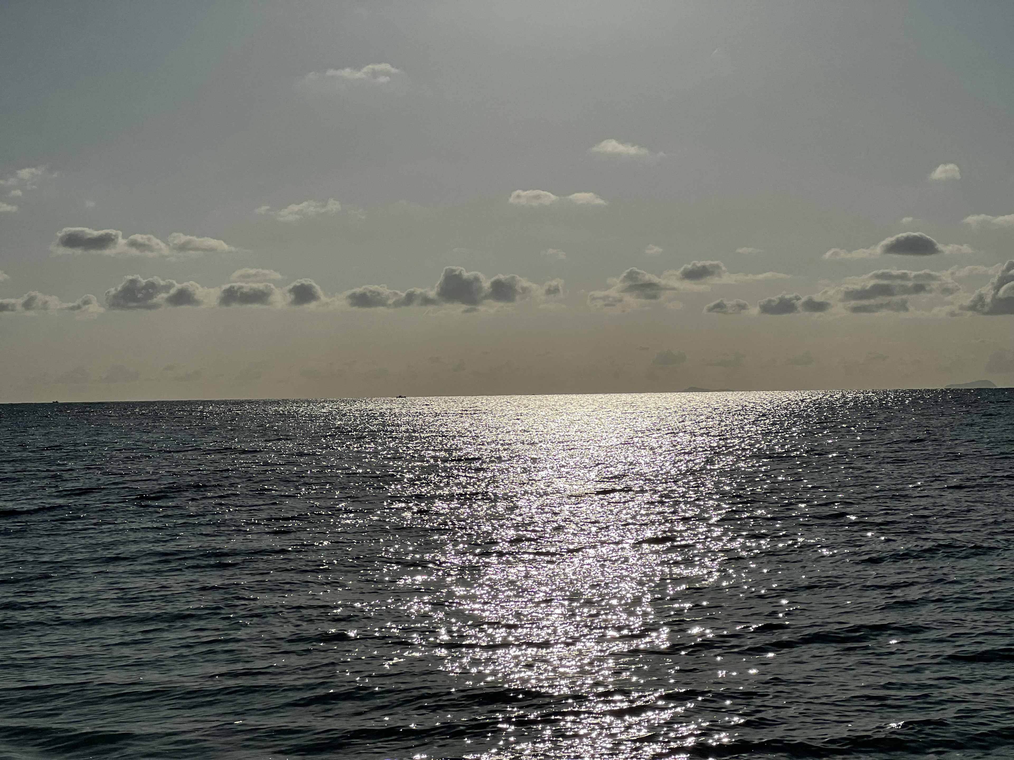 Paisaje marino tranquilo con luz del sol reflejándose en la superficie del agua y nubes en el cielo