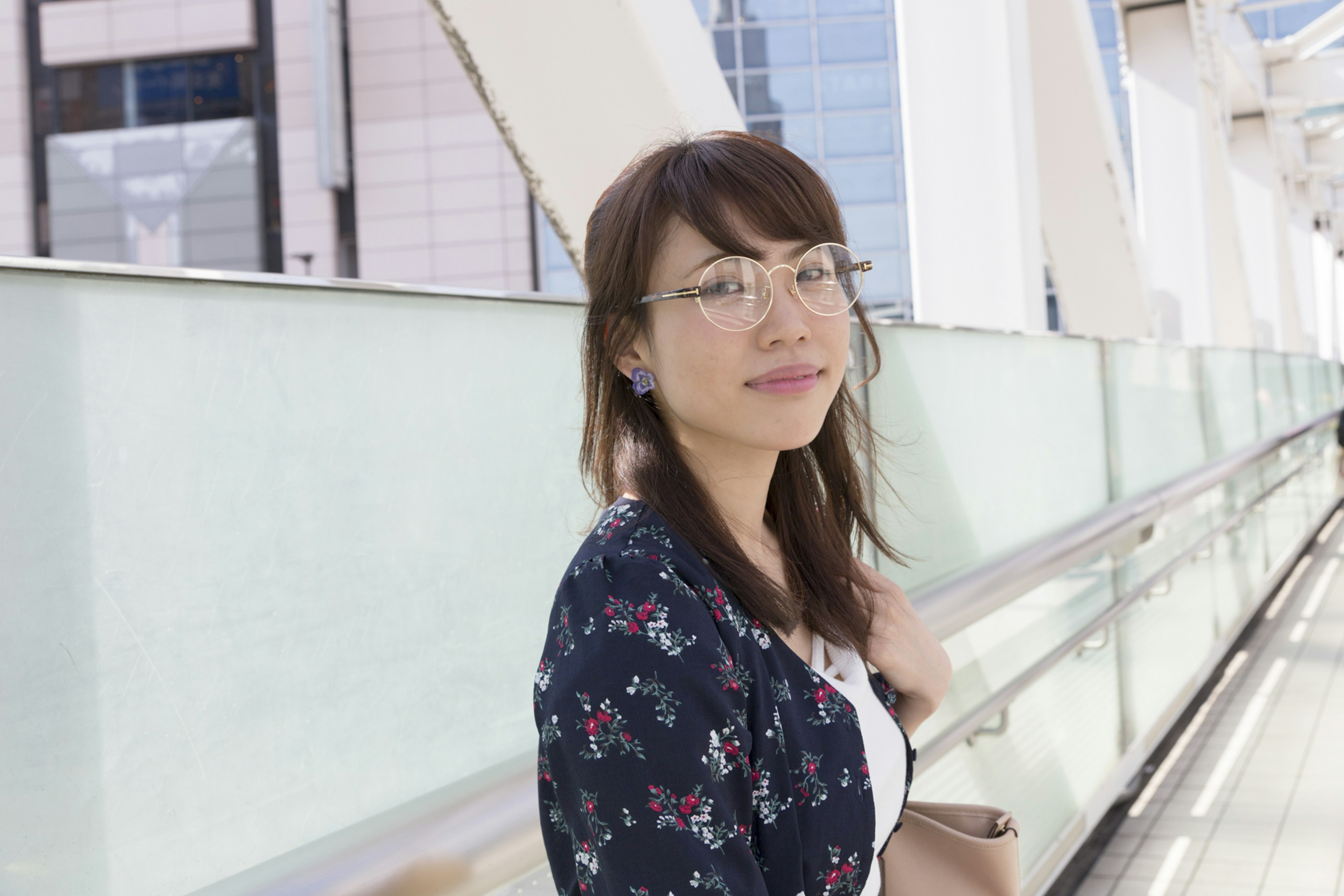 Eine Frau mit Brille lächelt mit modernen Gebäuden im Hintergrund