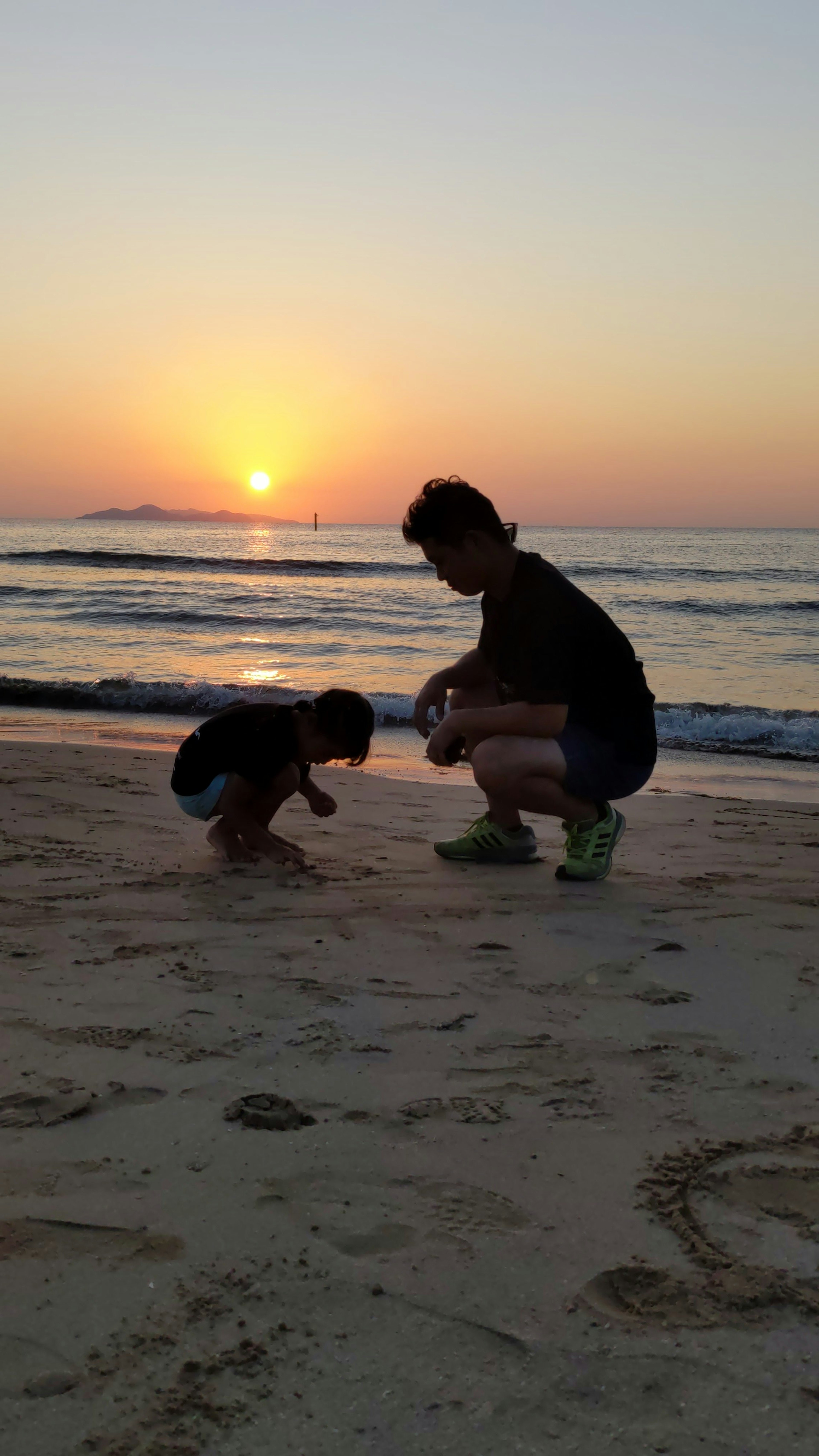 Silhouette di un genitore e un bambino che giocano sulla spiaggia al tramonto