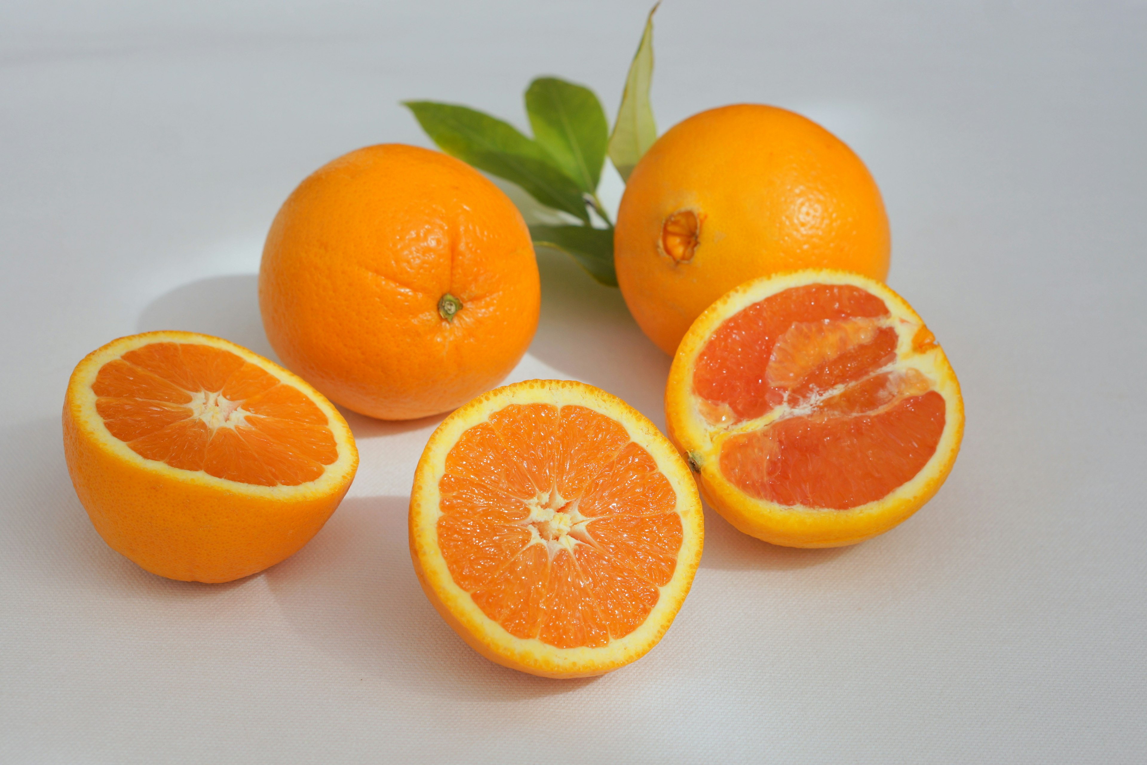 Image of oranges with one cut in half showing the juicy interior and green leaves