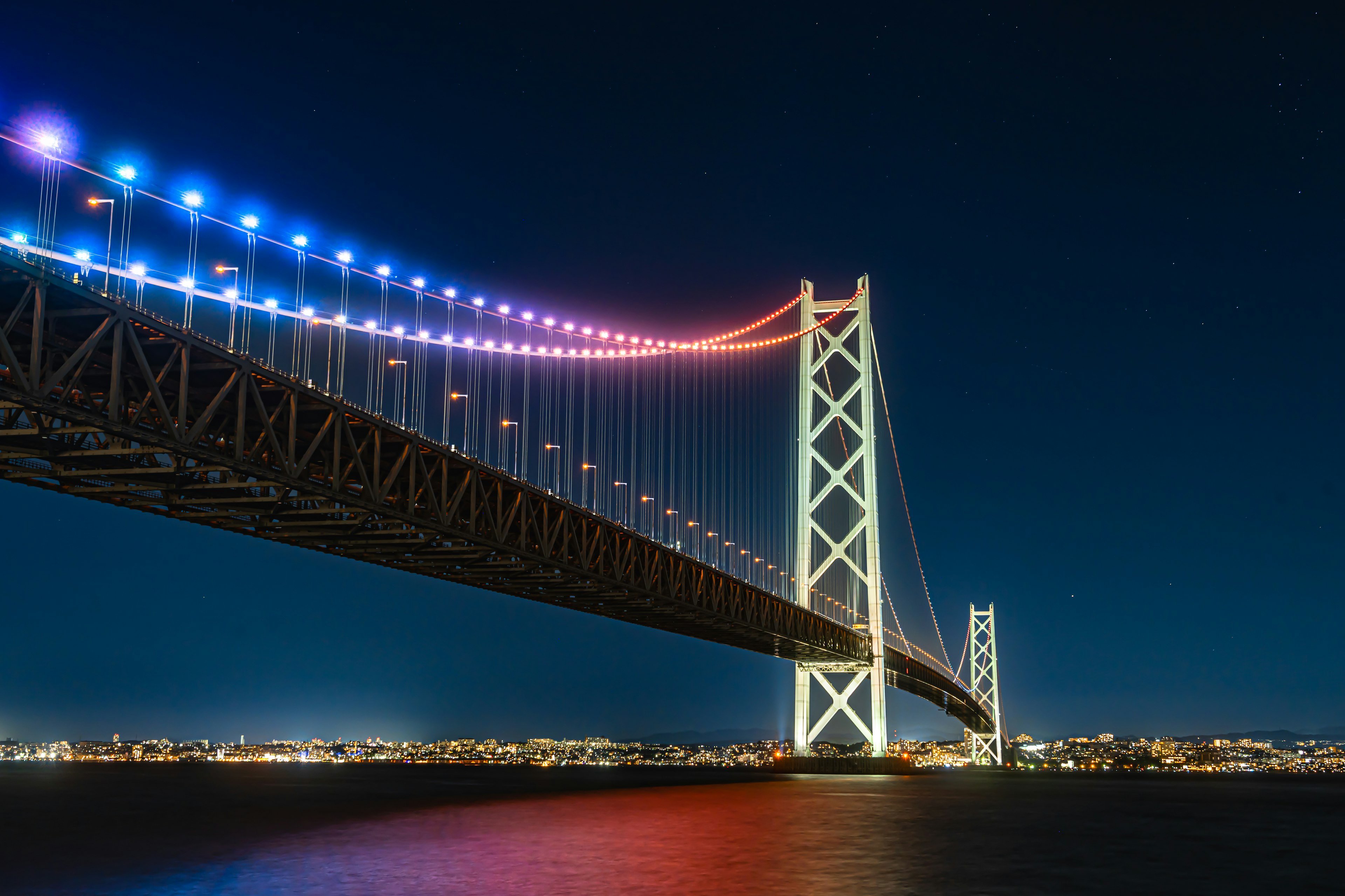 Pont illuminé s'étendant à travers un ciel nocturne sombre avec des lumières de la ville