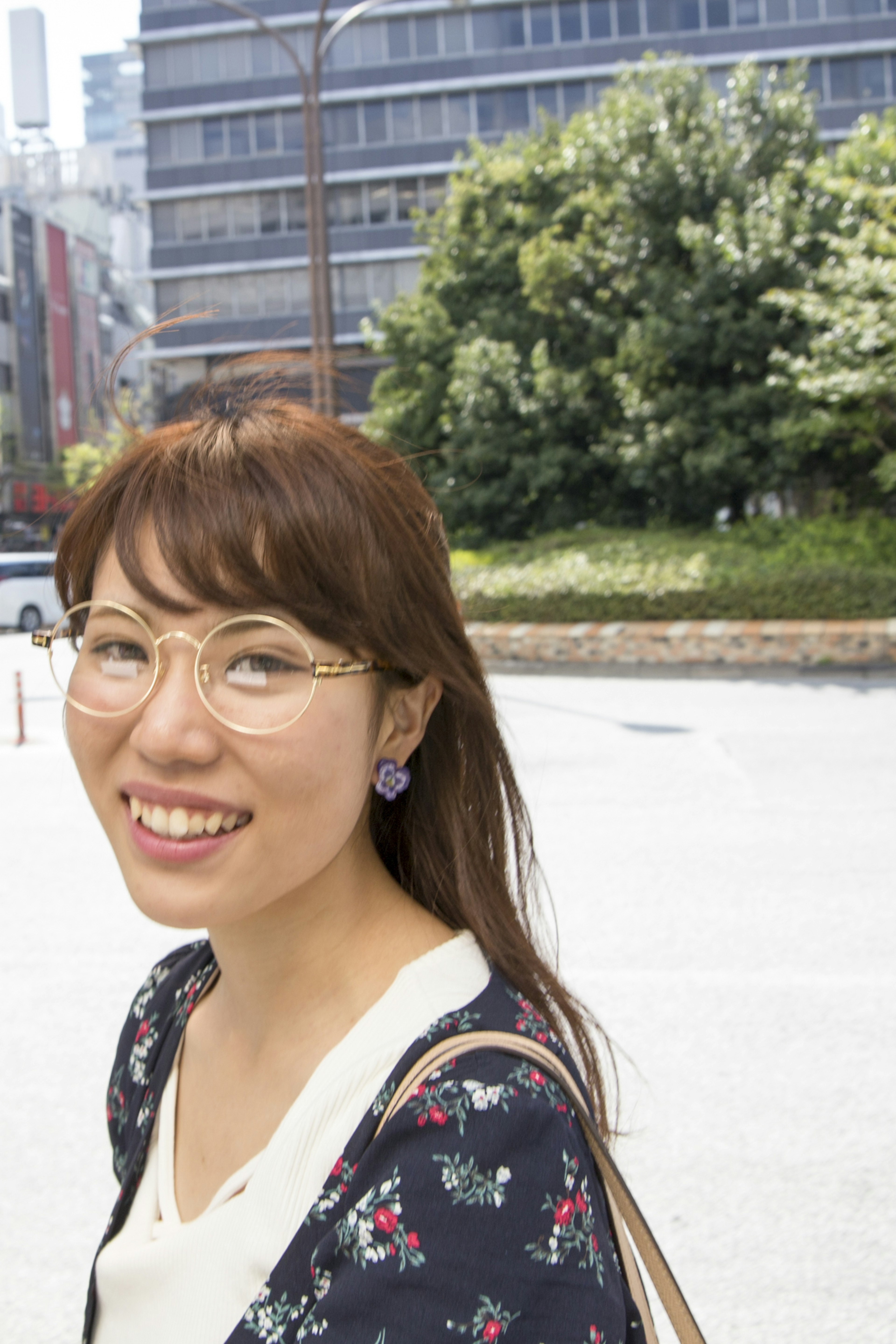 公園の緑を背景に笑顔の女性がメガネをかけている