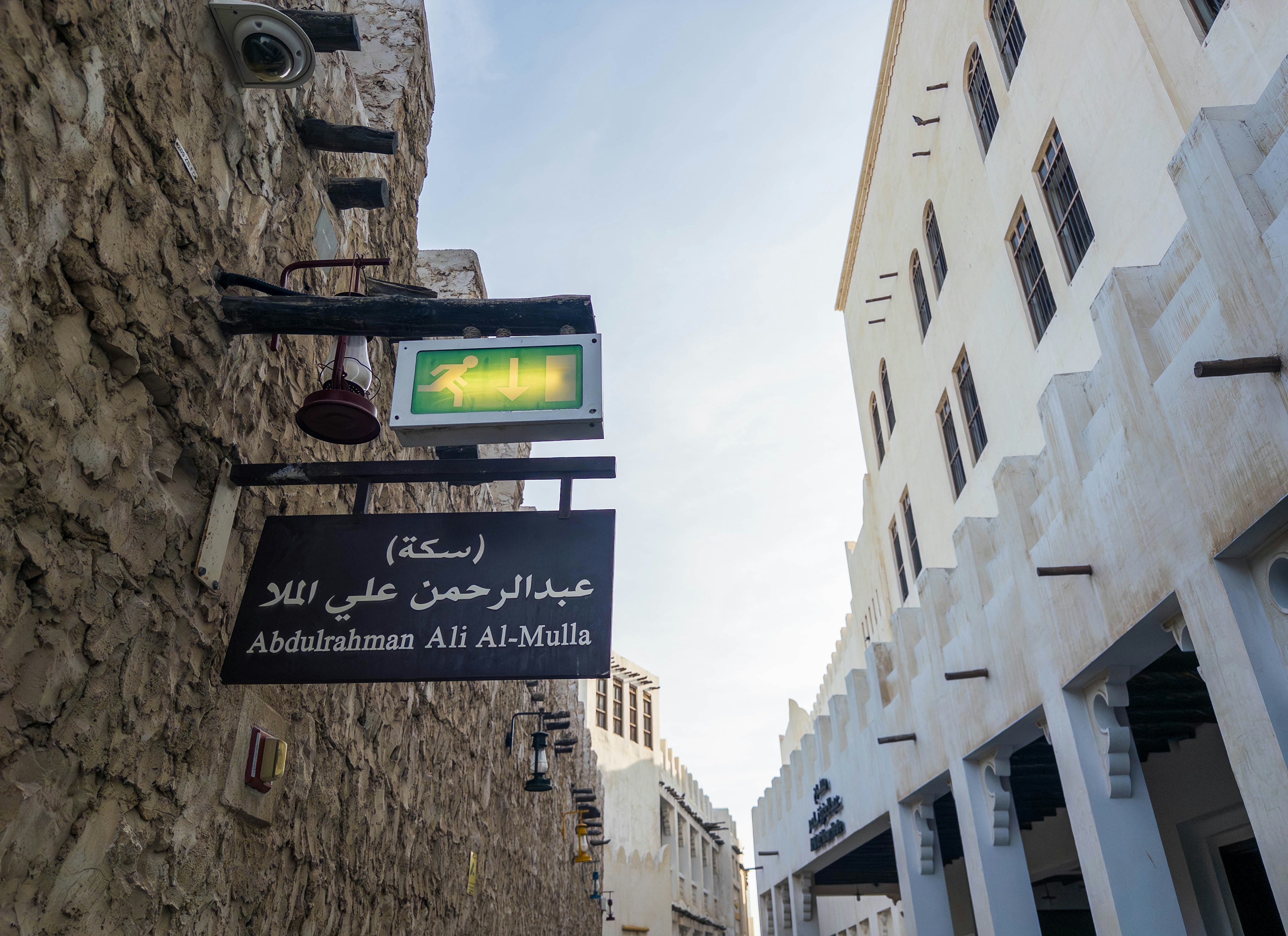 Street view featuring a sign in Arabic with stone walls and white buildings