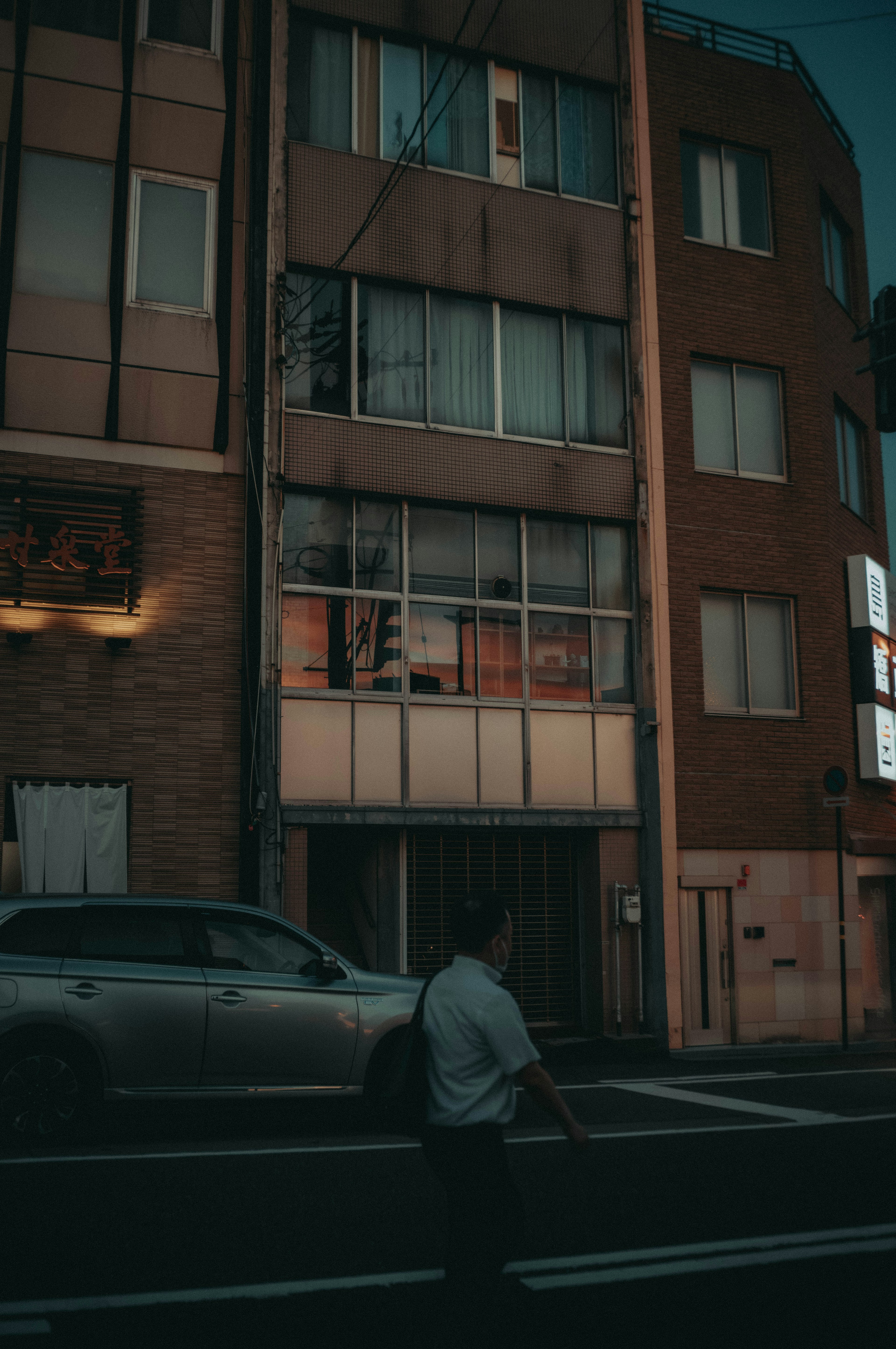 Escena de calle débilmente iluminada con un edificio y la silueta de un peatón