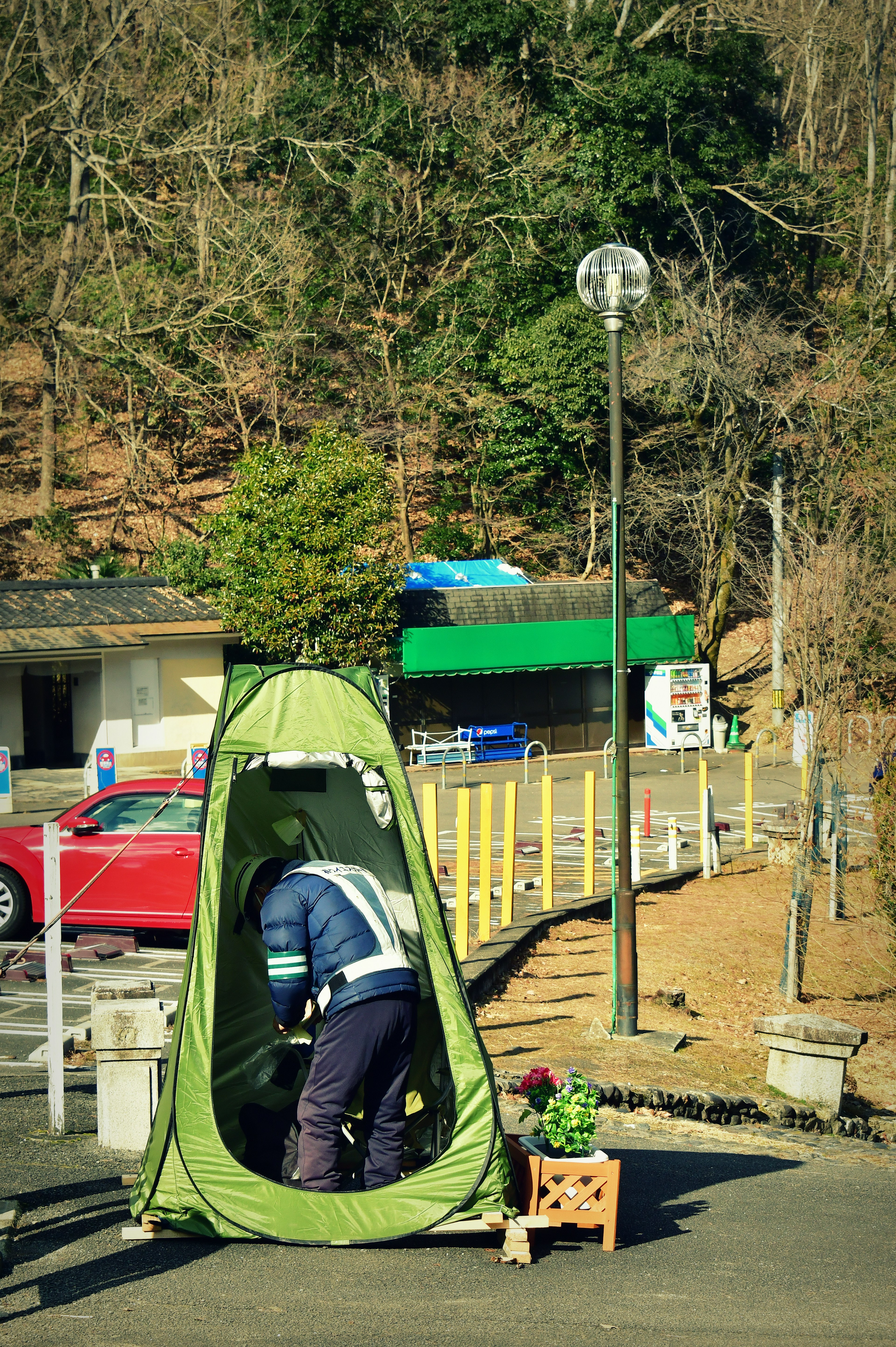 Person working inside a green tent with trees and a car nearby