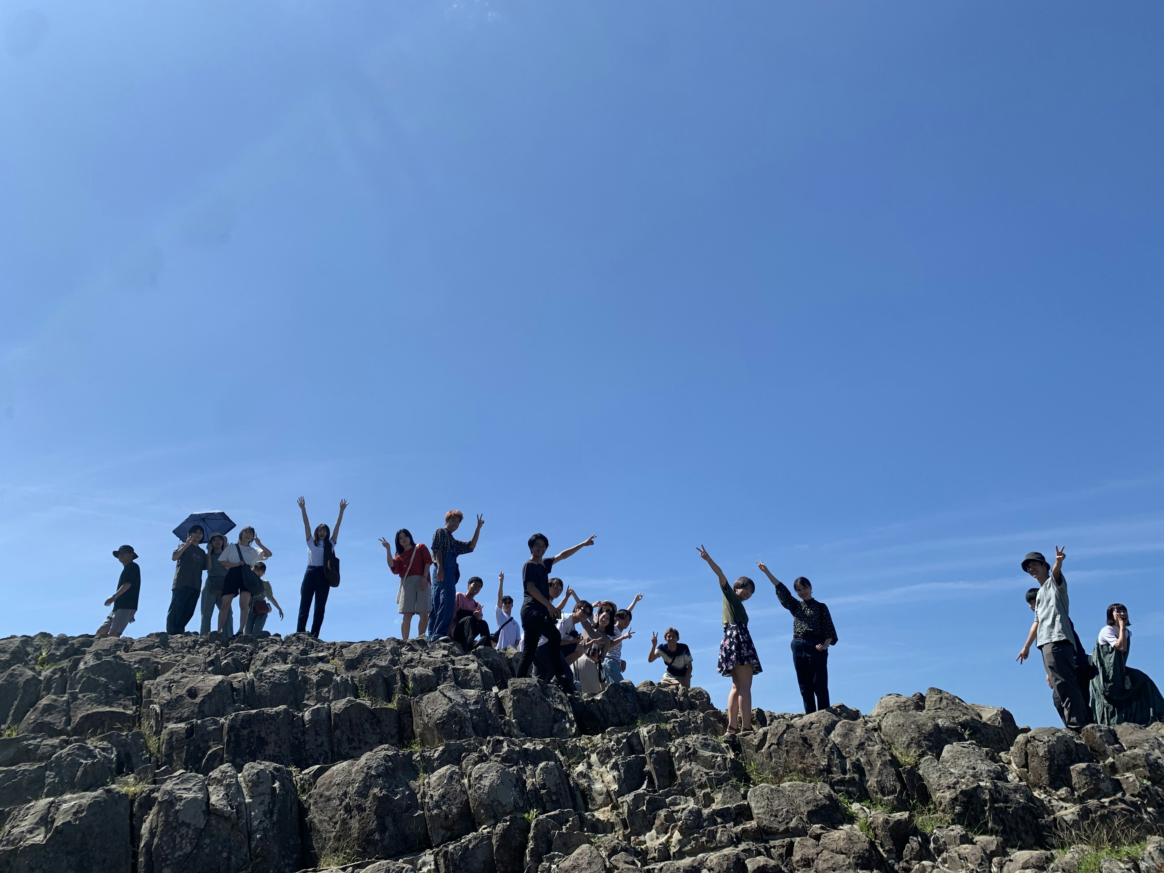 Groupe de personnes agitant la main sur un terrain rocheux sous un ciel bleu clair