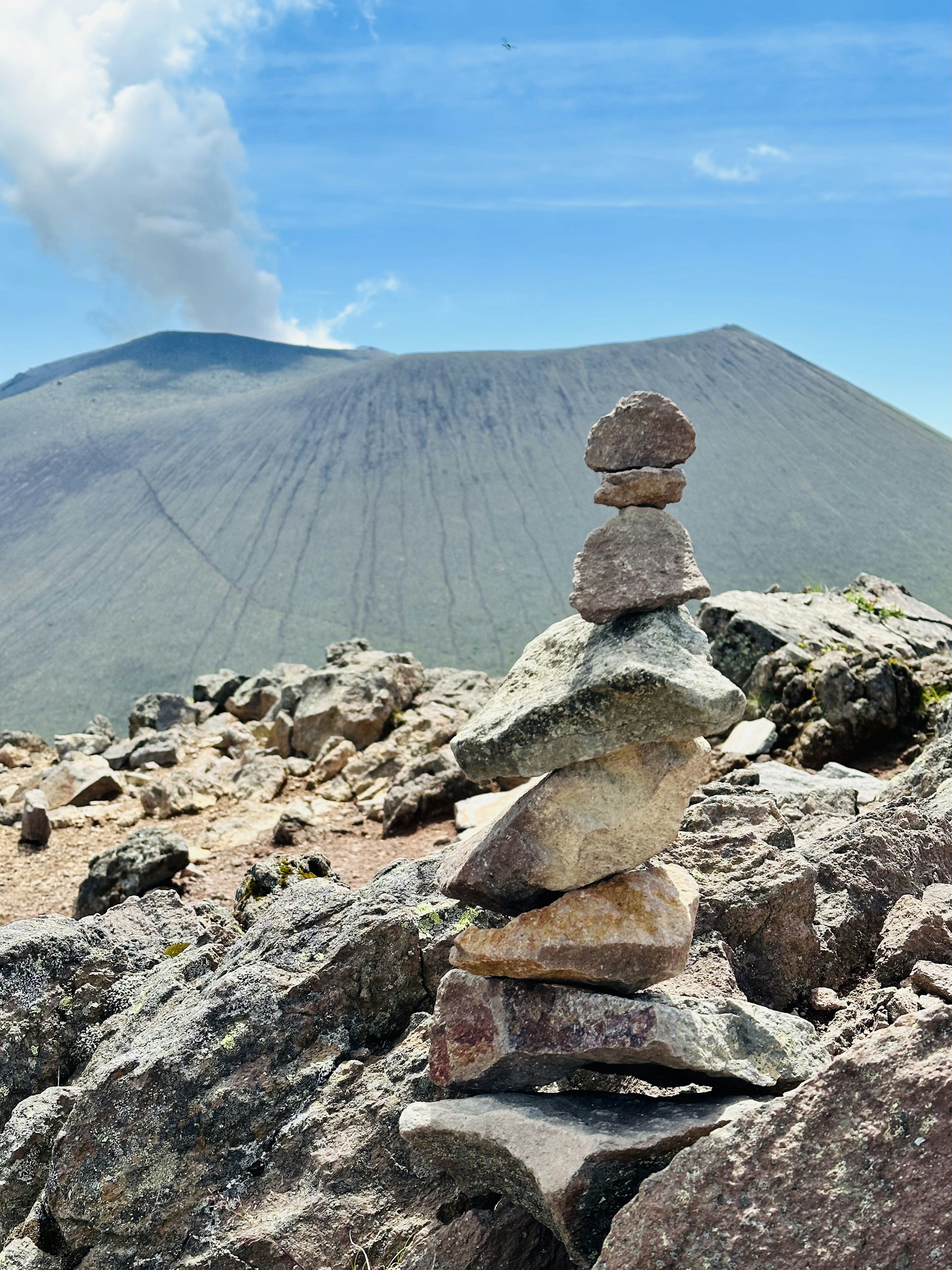 Pila de piedras en una montaña con un volcán al fondo