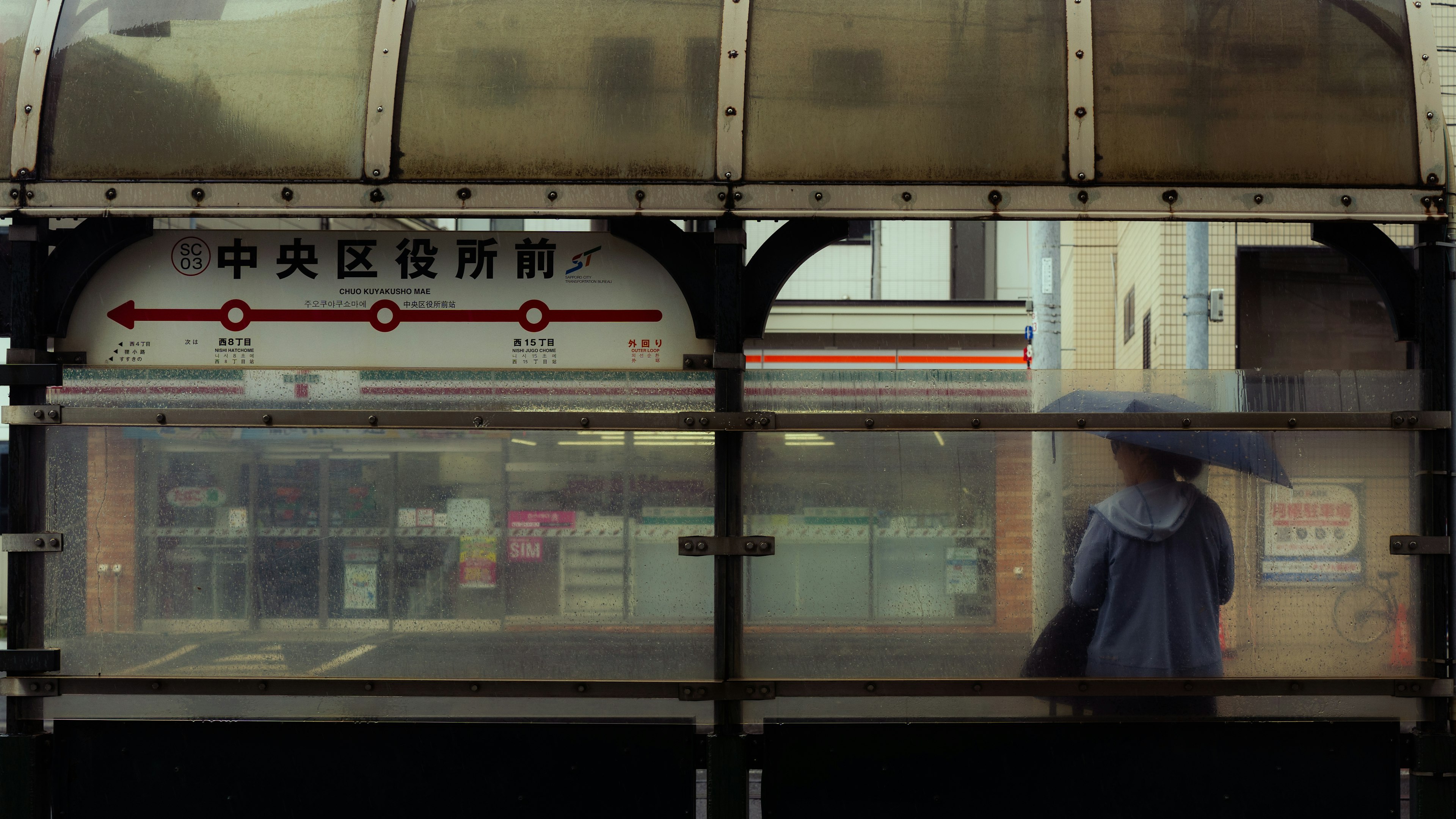 雨の中で傘を持つ人が見えるバス停の風景