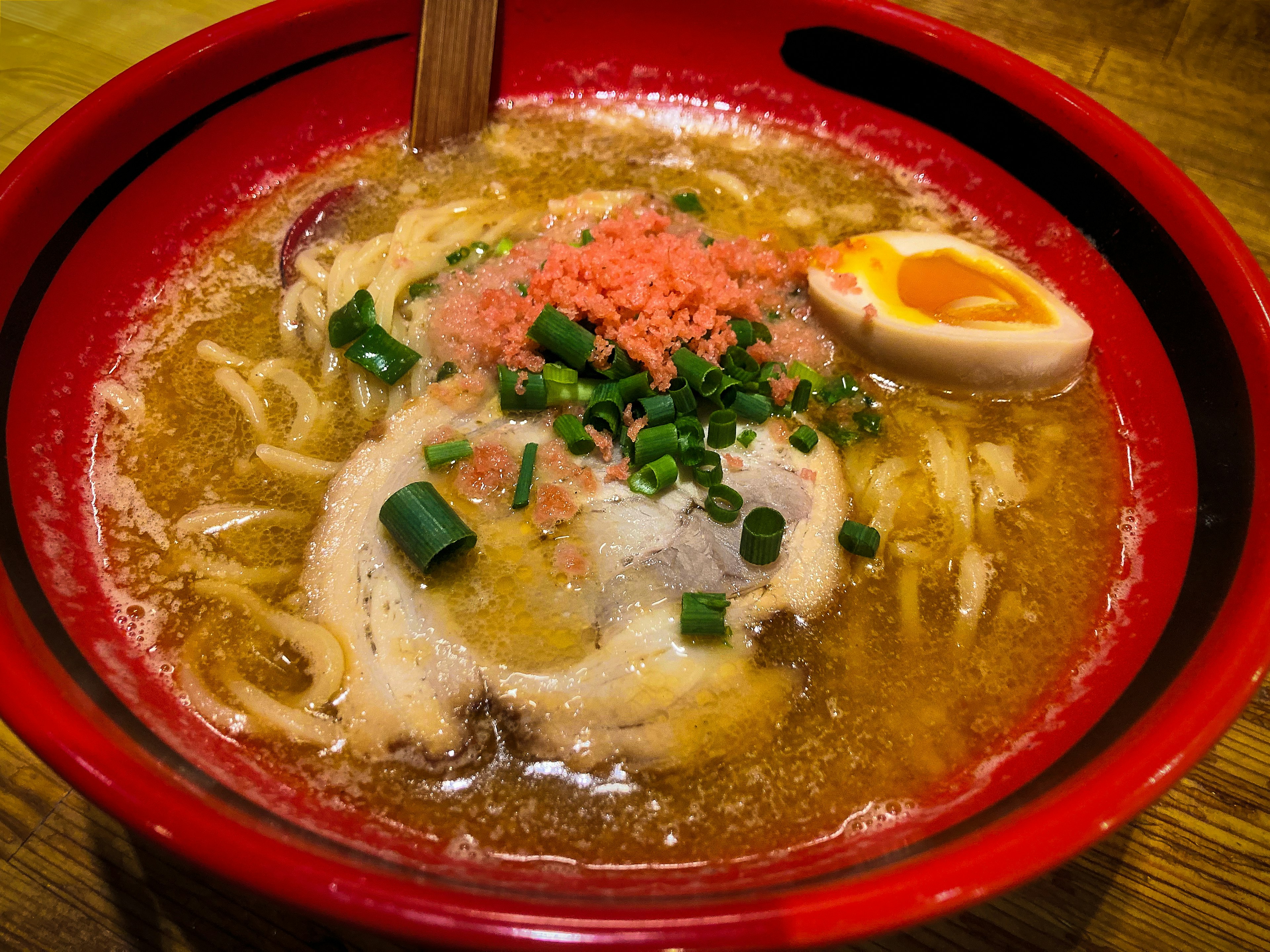 赤い丼に盛られたラーメンにチャーシュー、煮卵、ネギ、かつおぶしがトッピング