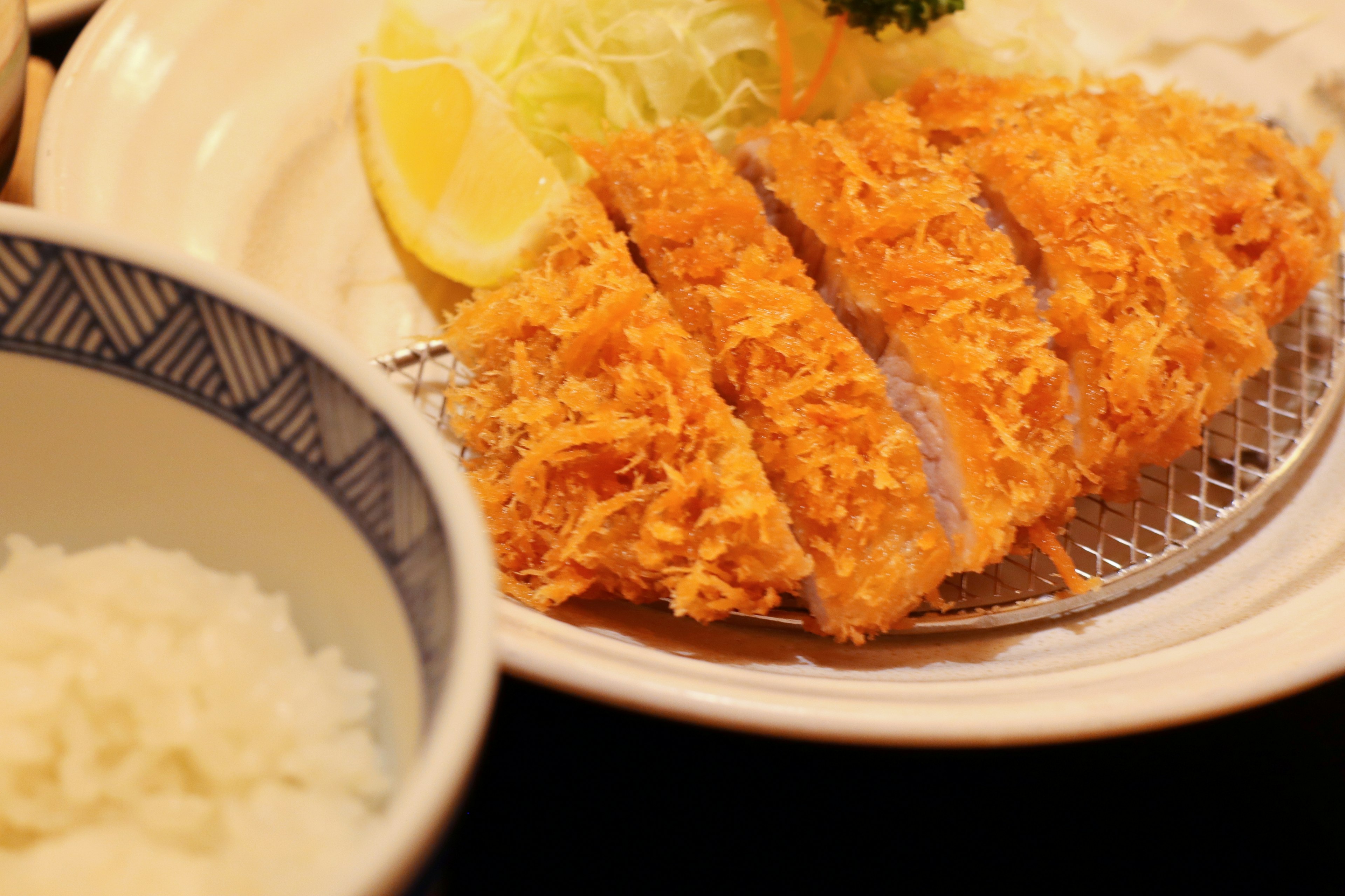 Tonkatsu crujiente en rodajas en un plato con guarnición de limón y repollo