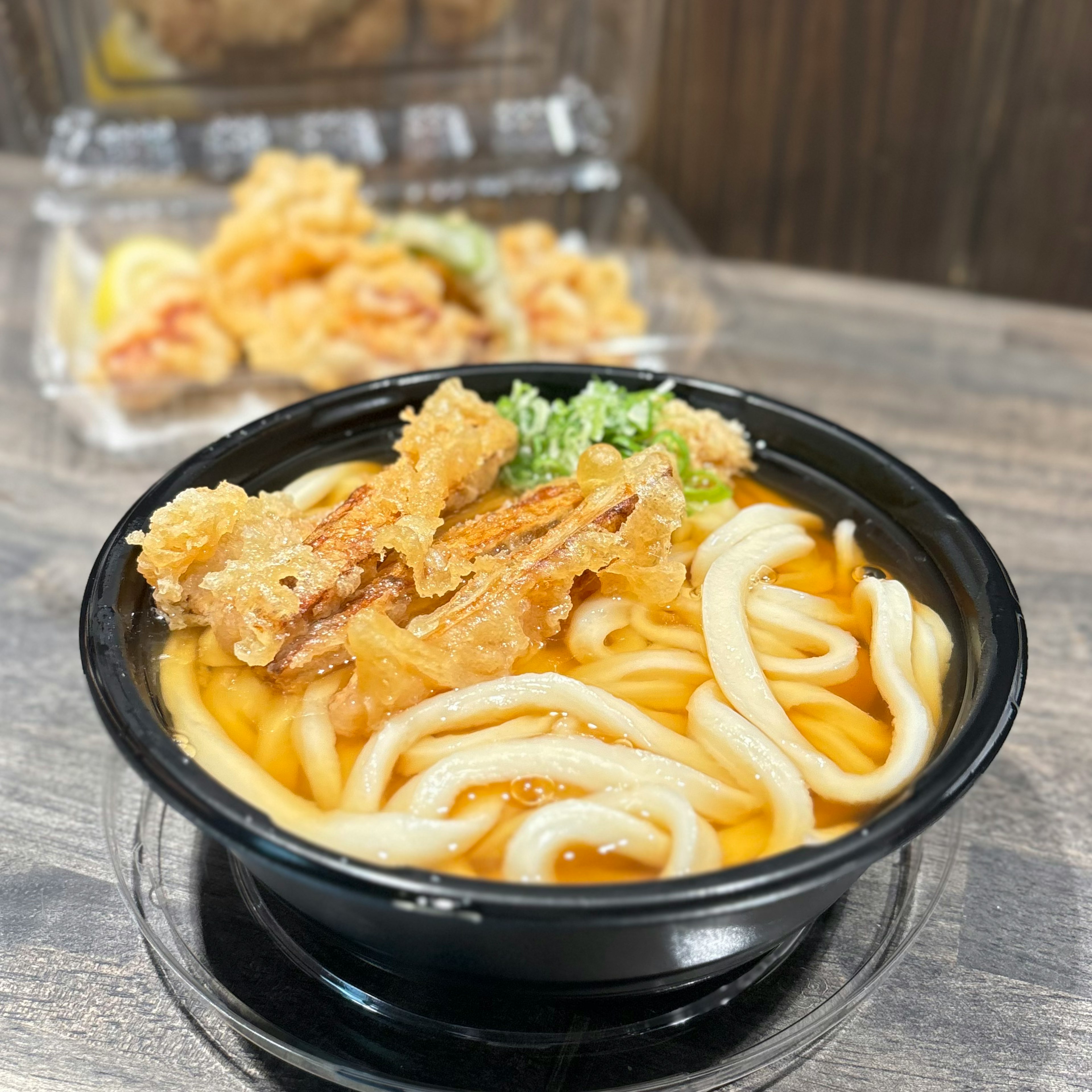 うどんと天ぷらの盛り合わせが入った黒い容器の料理