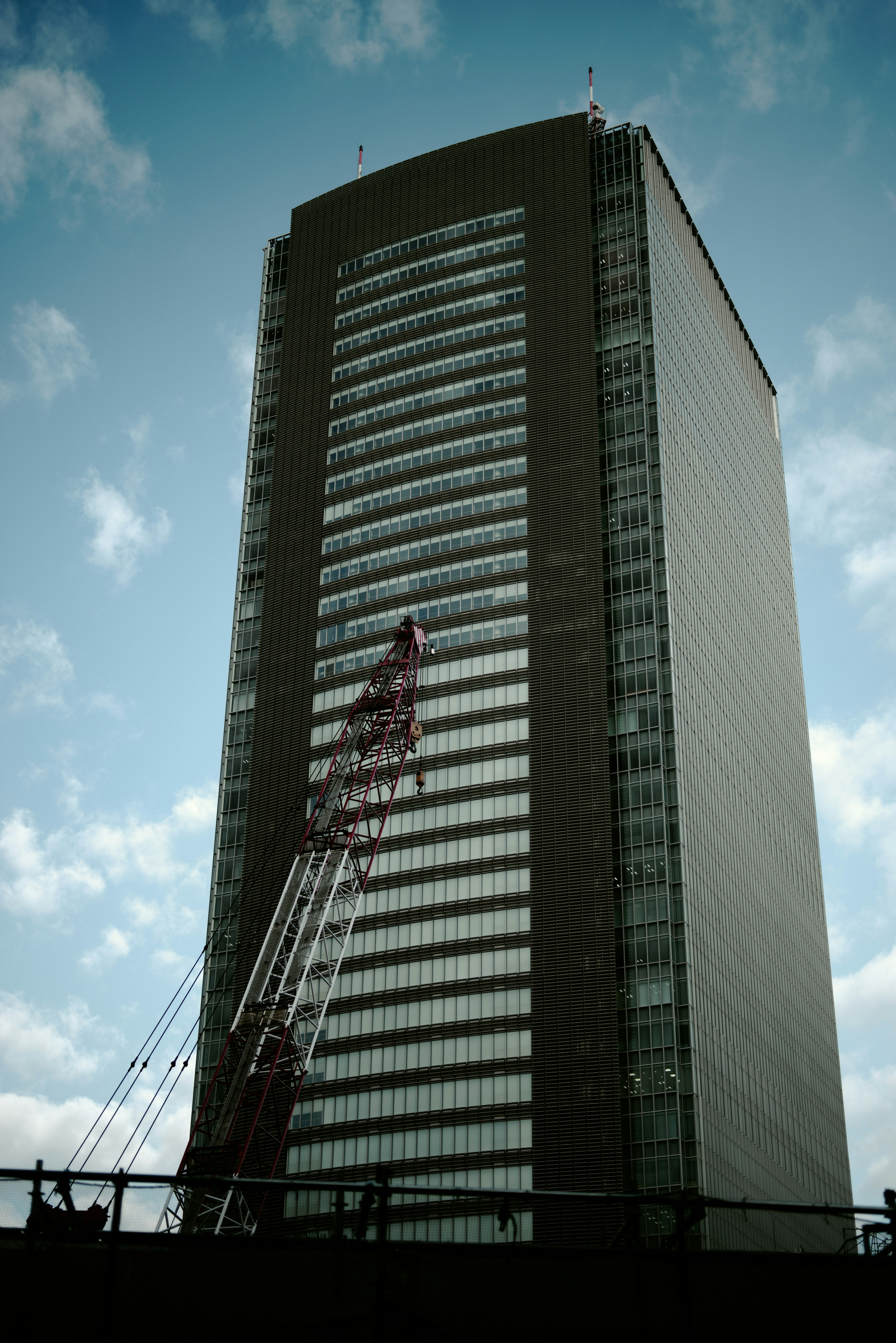 View of a skyscraper with a crane against a cloudy sky