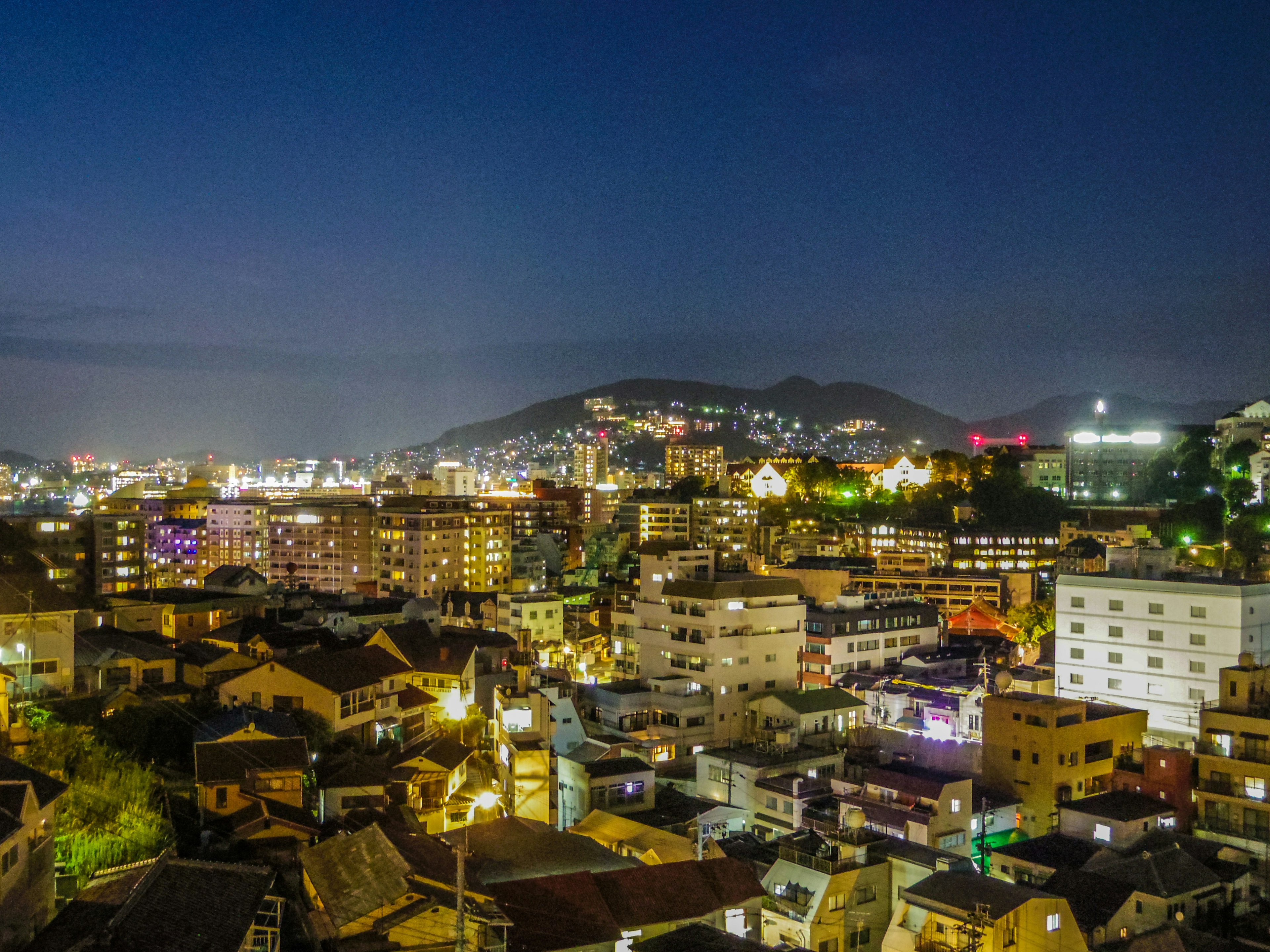 Paysage urbain nocturne avec bâtiments illuminés et silhouette de montagne