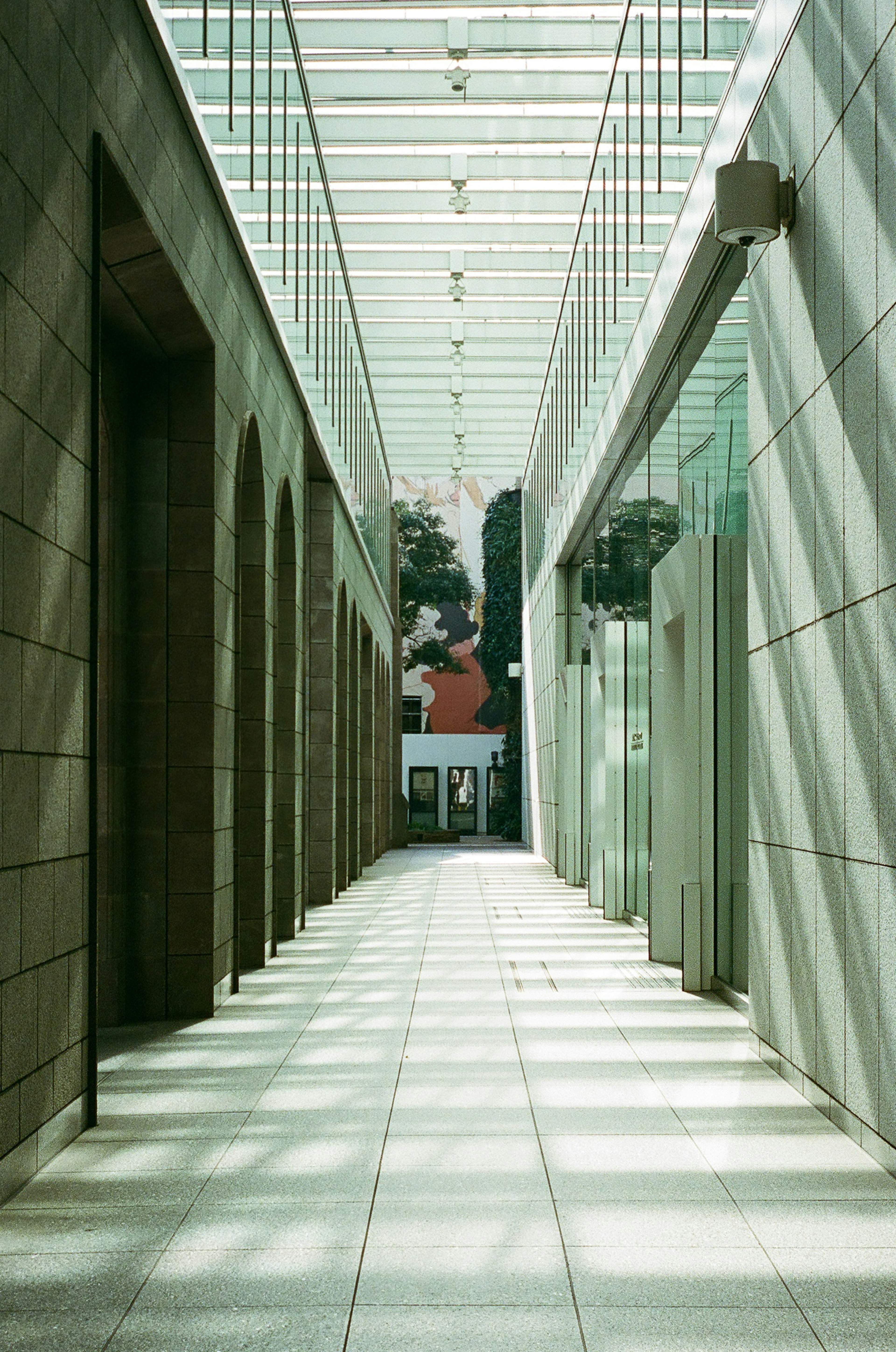 Vista interior moderna de un pasillo con techo de vidrio y paredes de piedra que permiten el paso de la luz