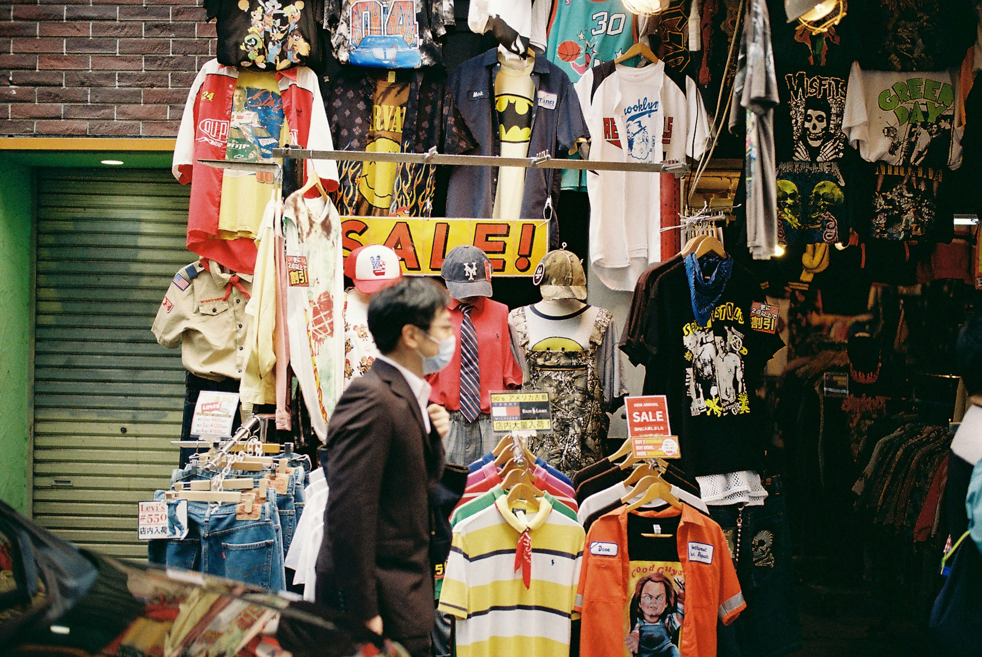 Homme marchant devant un magasin de vêtements en plein air rempli de t-shirts colorés