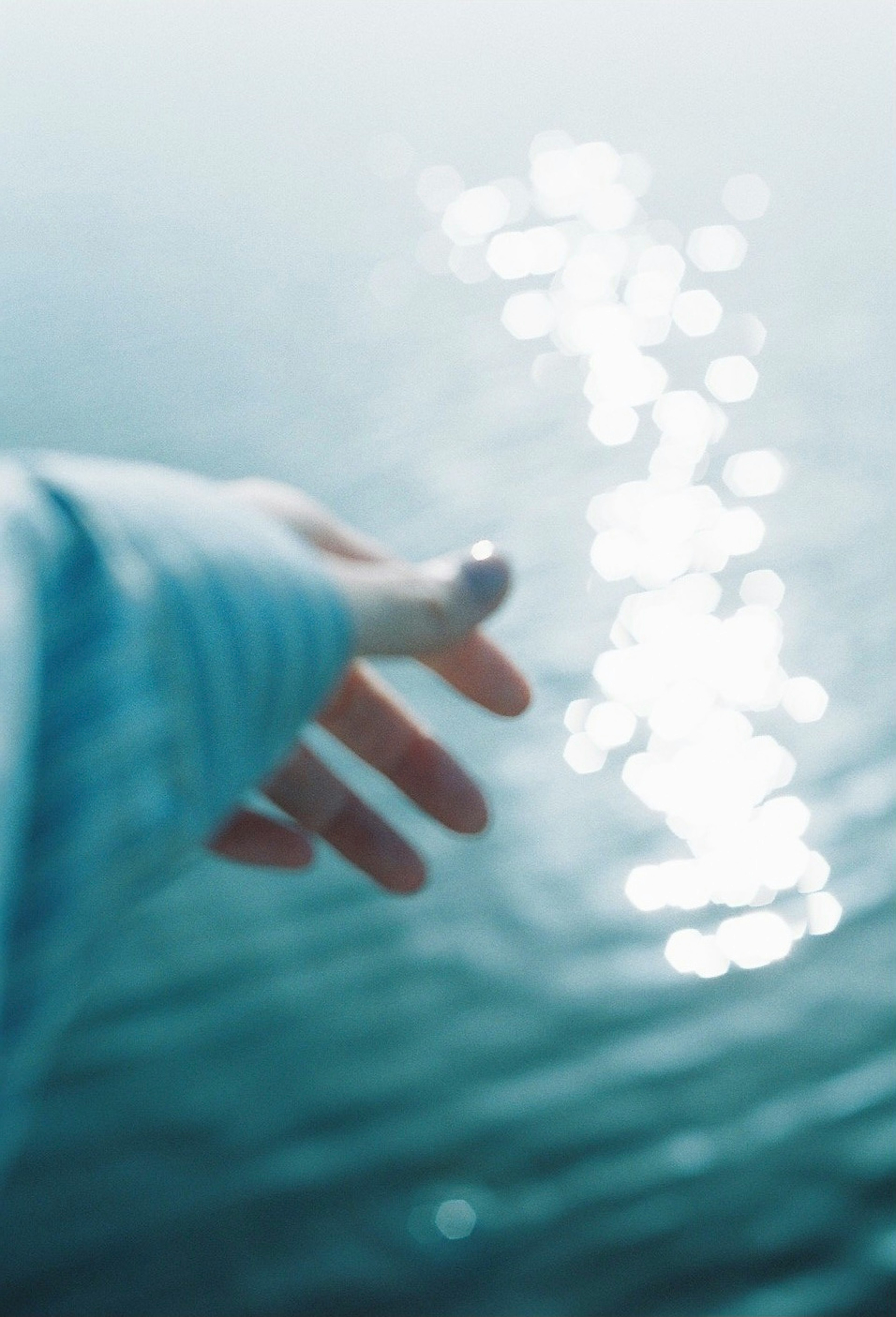 Close-up shot of a hand reaching towards the water surface with shimmering light reflections