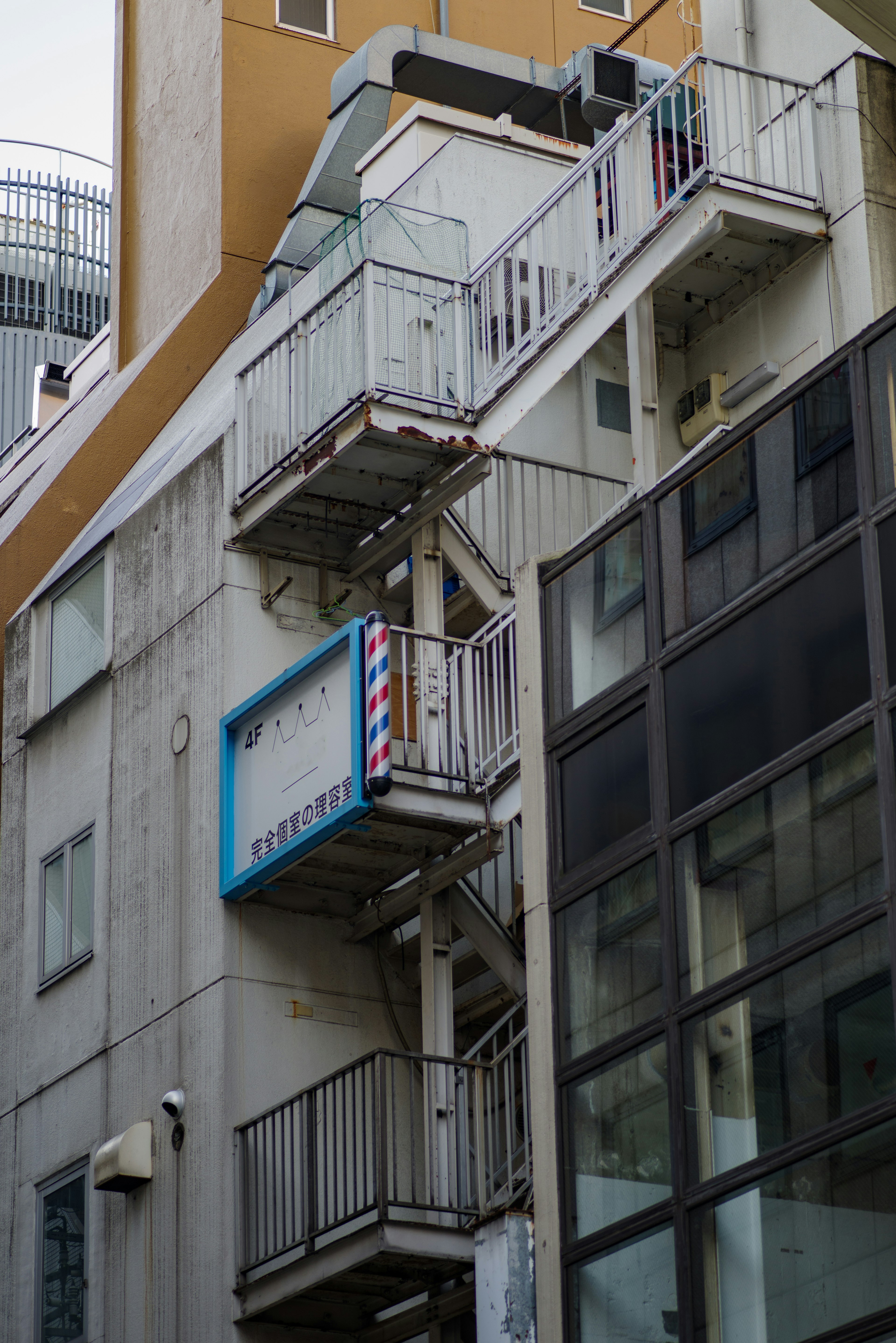 白い外壁とガラスのビルが並ぶ街並みに、青い看板の理髪店の階段が見える