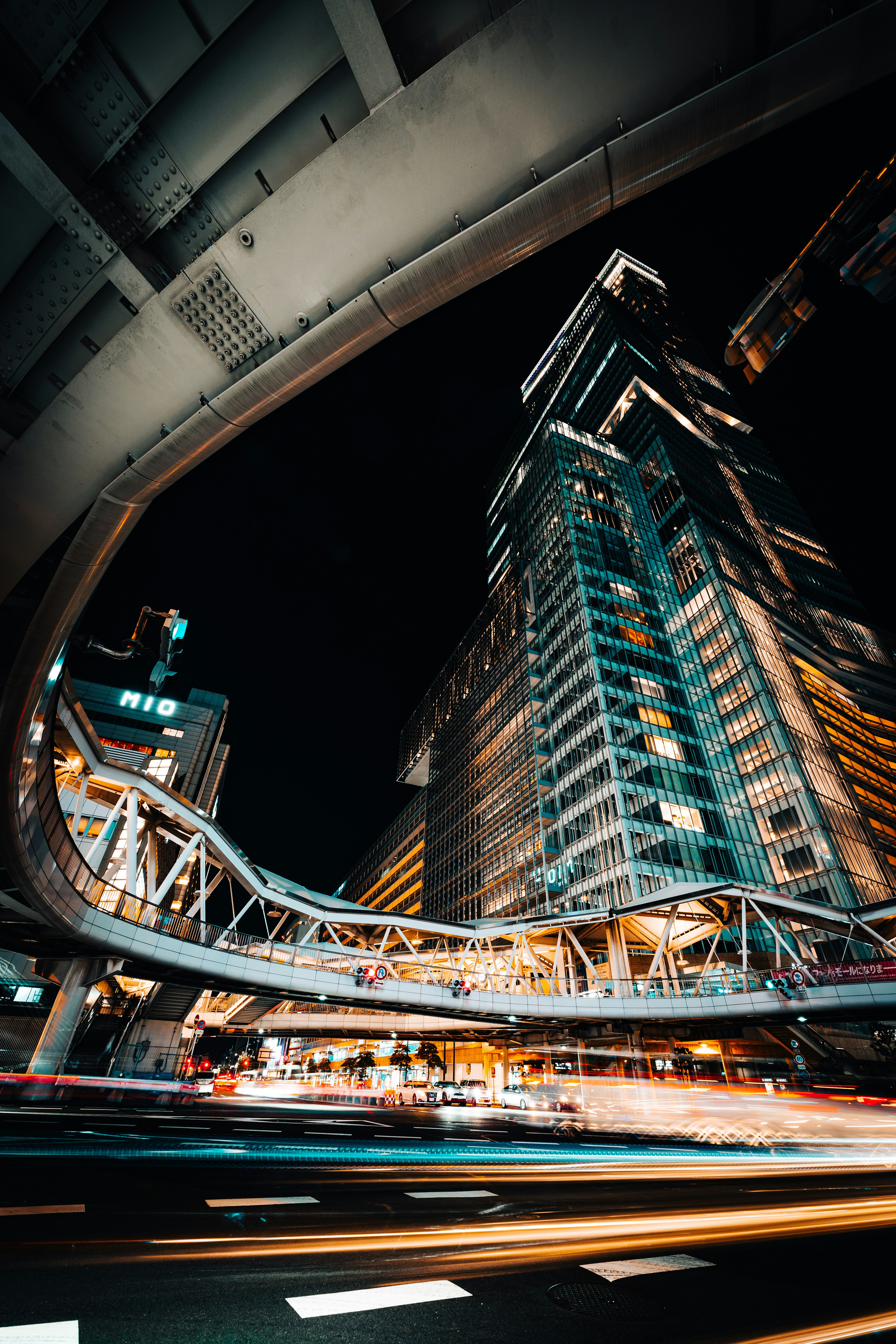 Scène urbaine nocturne avec un bâtiment de grande hauteur et un pont piéton courbé