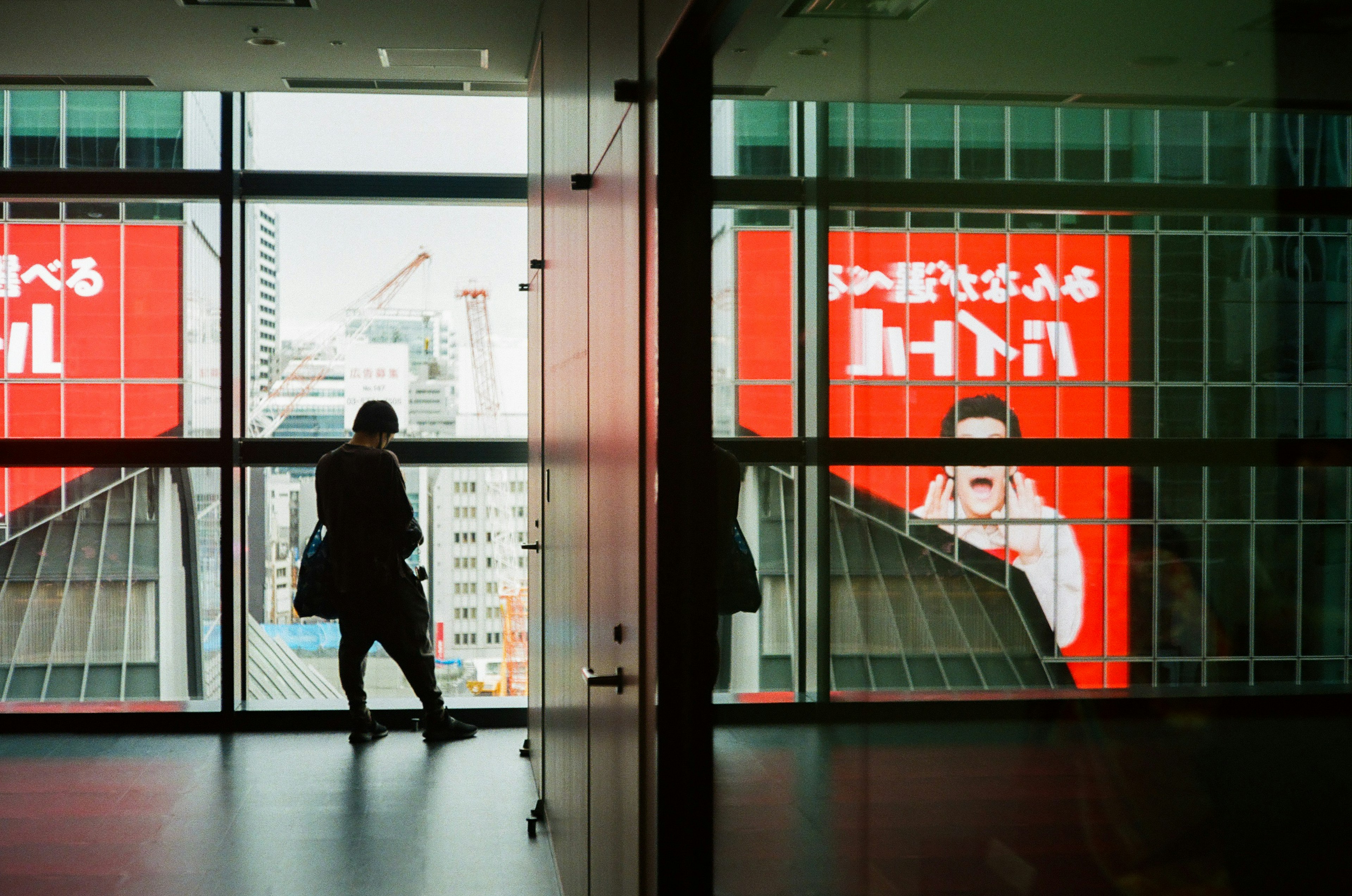 A silhouette of a person looking out a building window with red advertisements in view