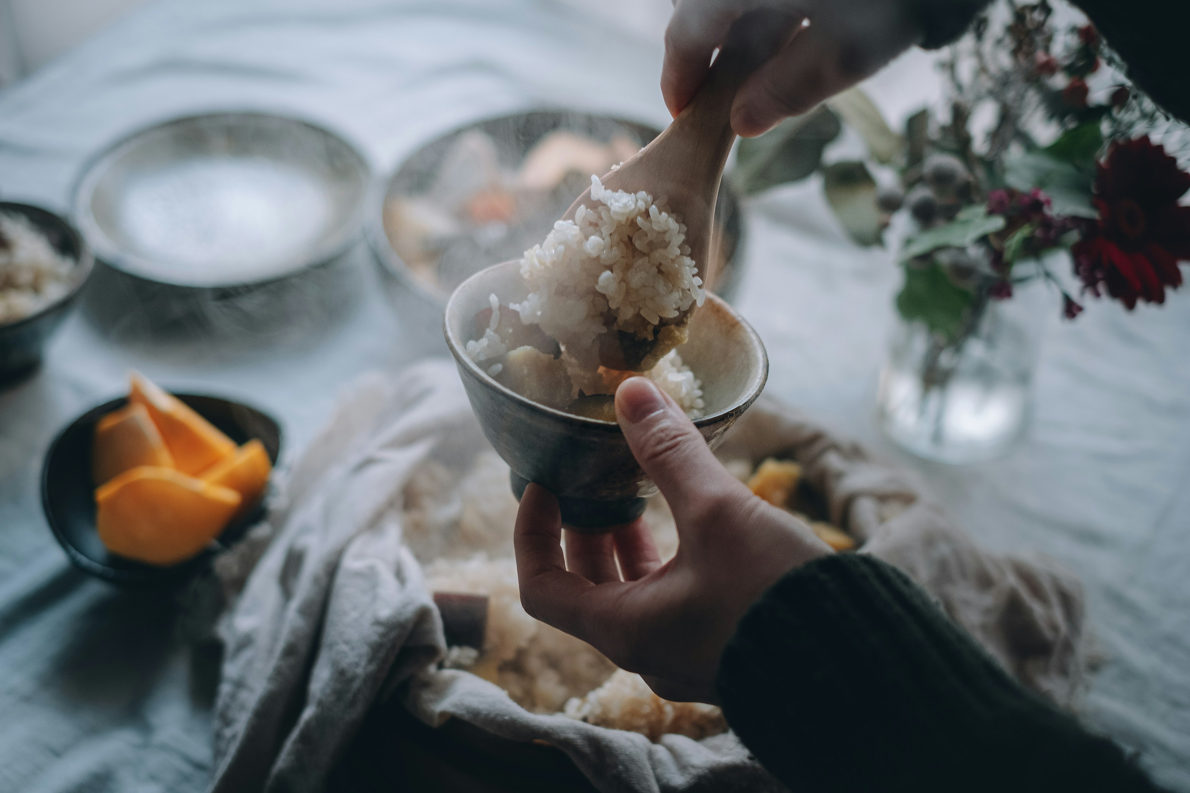 A person holding a bowl serving rice with flowers and fruit in the background