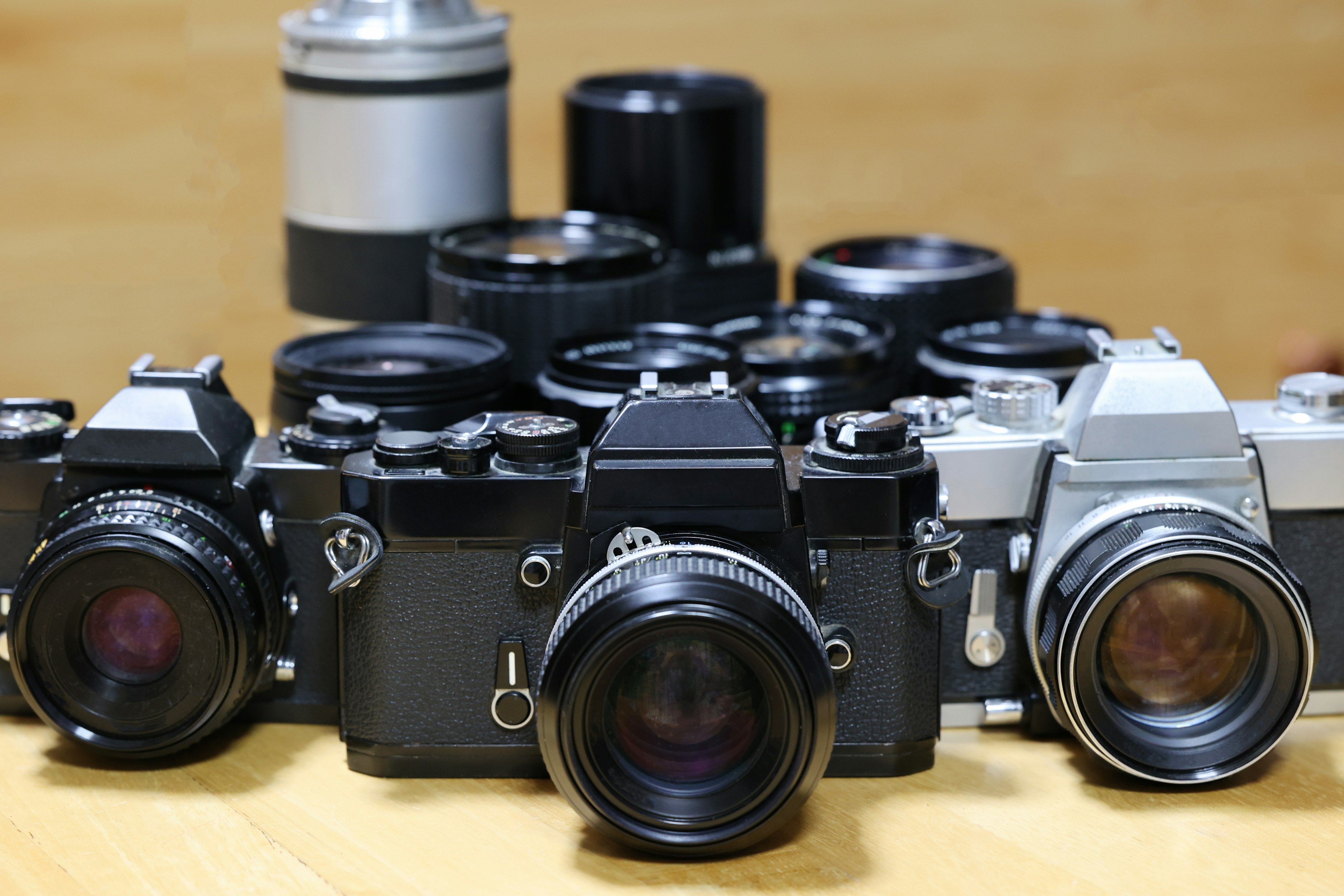 Still life of cameras and lenses featuring black and silver film cameras in the foreground with multiple lenses in the background