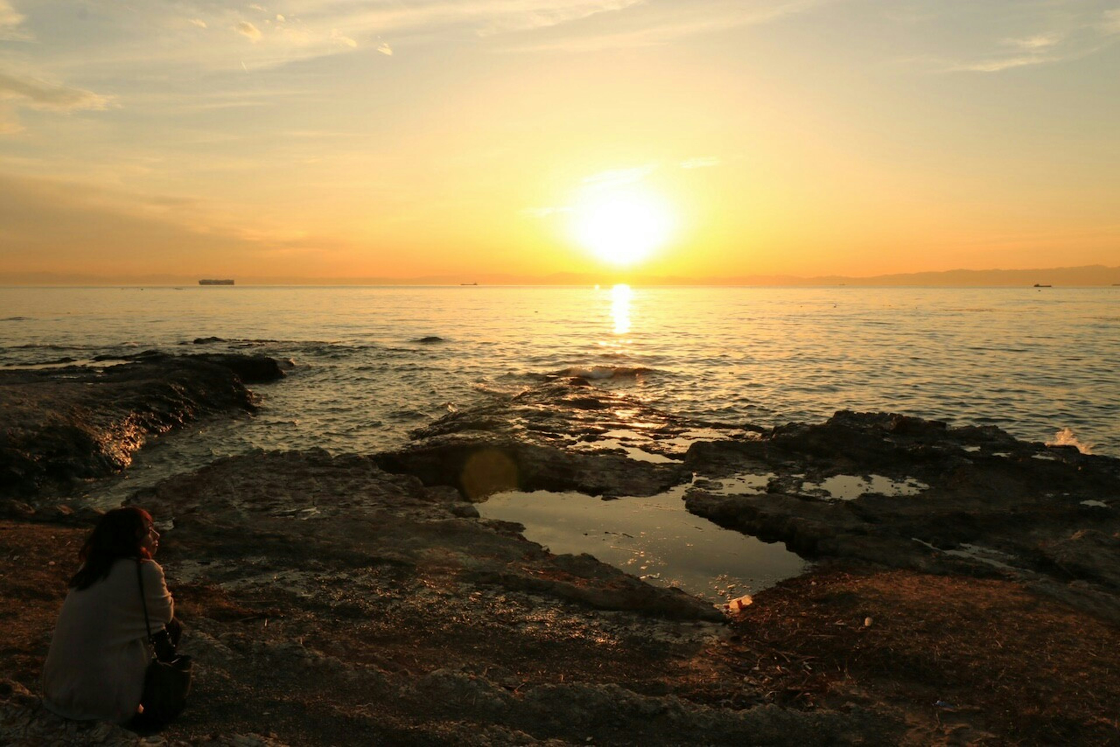 Silhouette einer Person, die den Sonnenuntergang an der Küste beobachtet schöner orangefarbener Himmel und ruhiges Meer