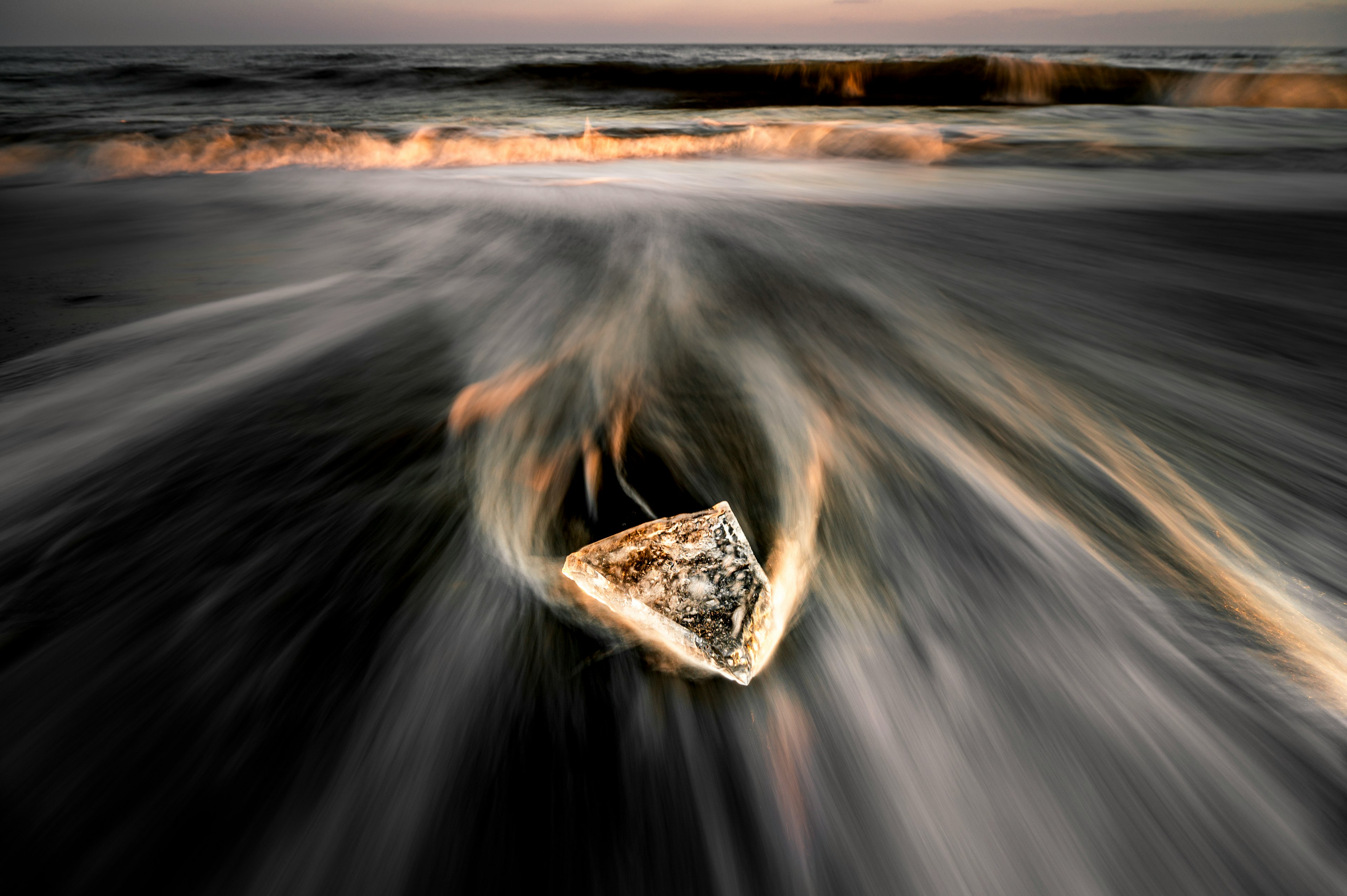 Un pezzo di ghiaccio trasparente che galleggia tra le onde con uno sfondo di oceano al tramonto