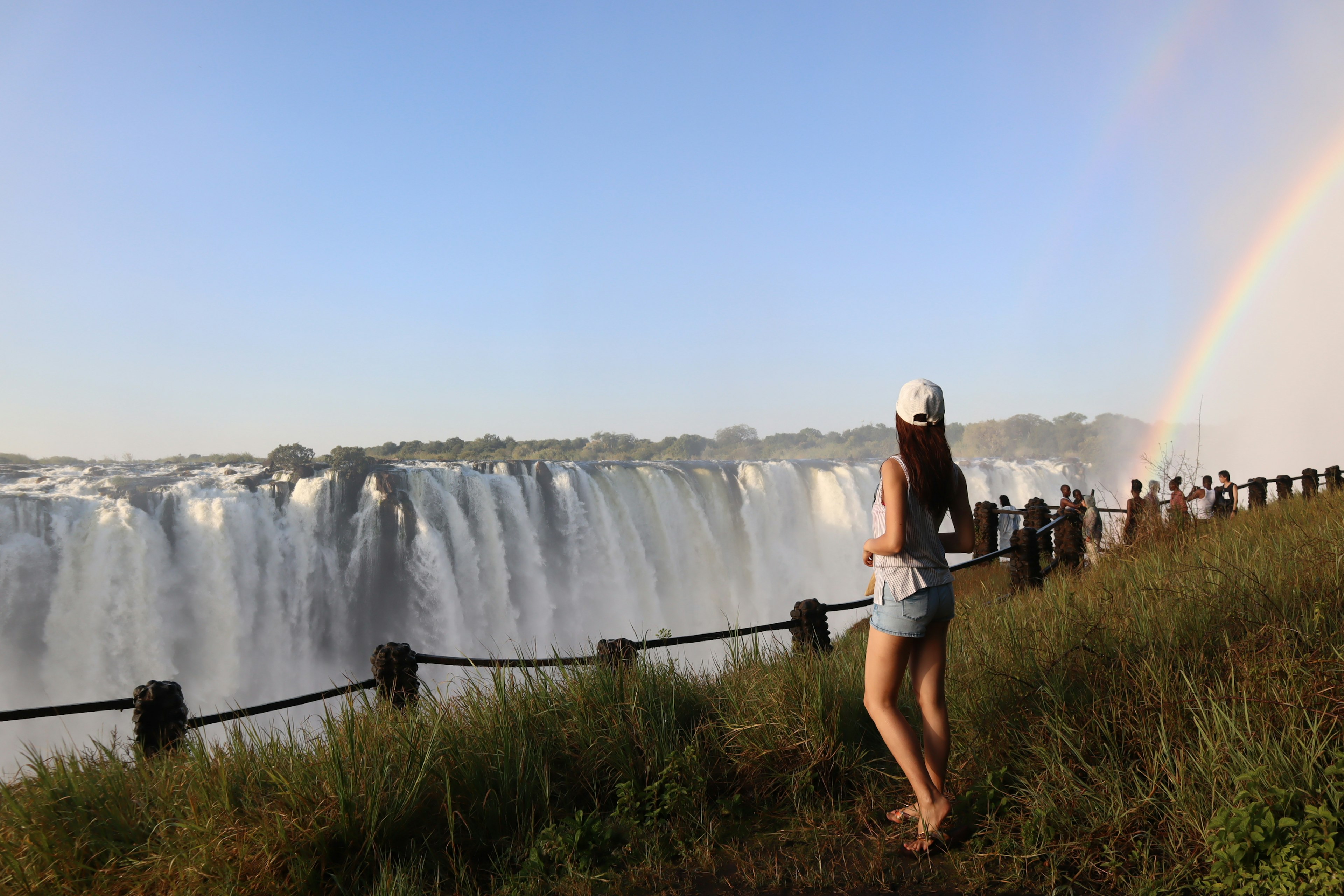 Mujer de pie cerca de una cascada con un arcoíris al fondo