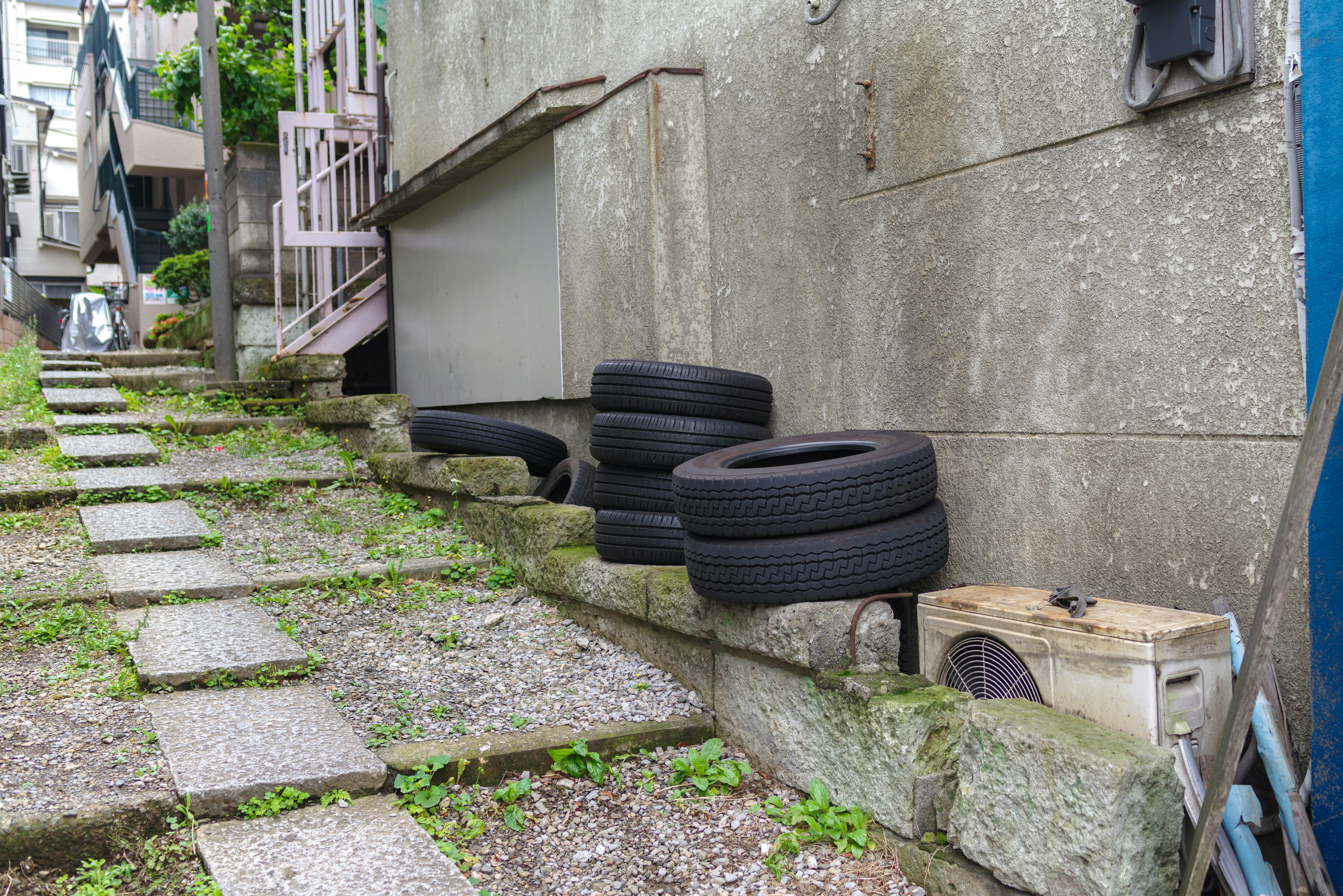 Black tires stacked beside a paved walkway with greenery