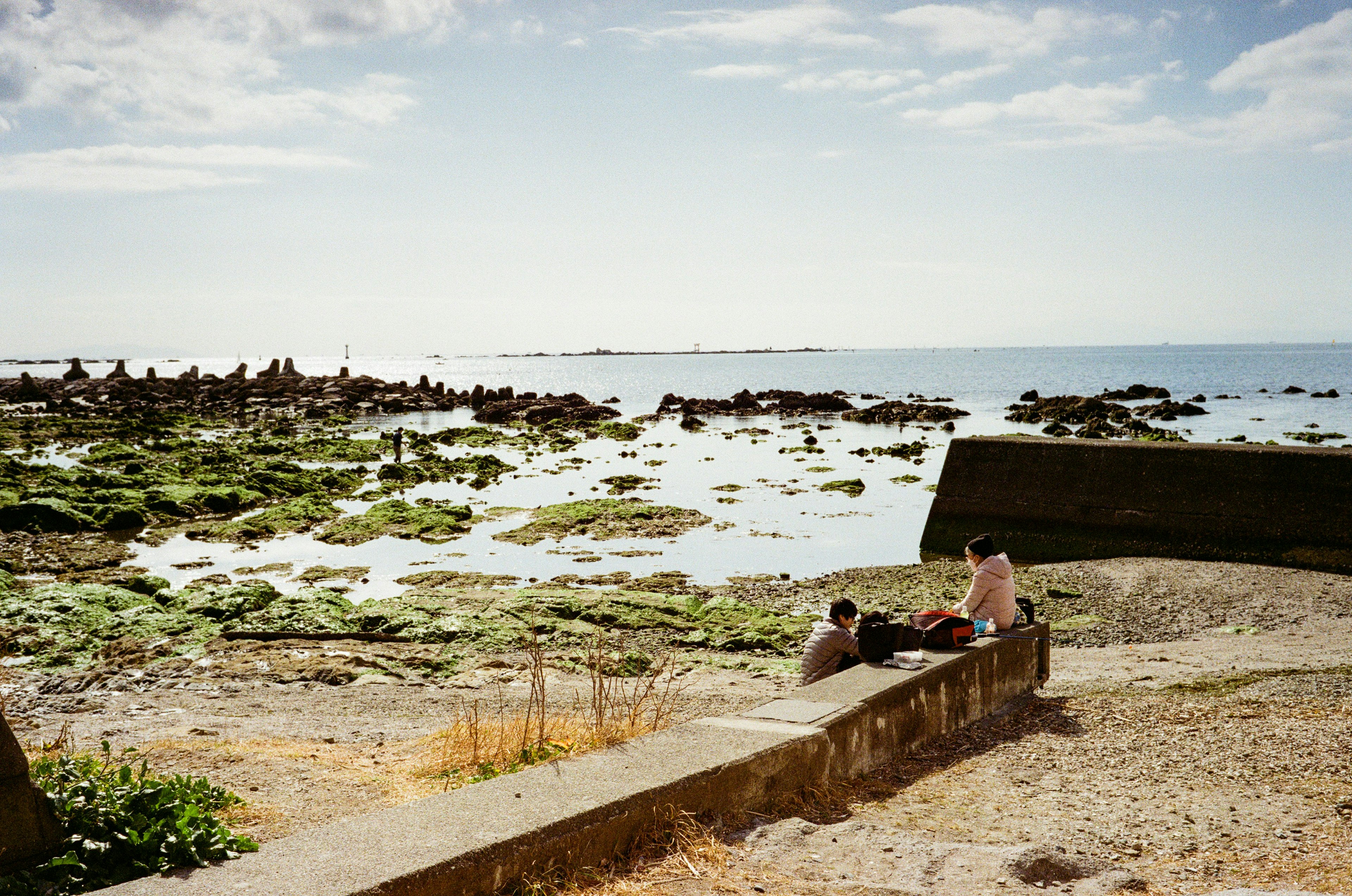 Two people sitting on a coastal wall with a scenic ocean view