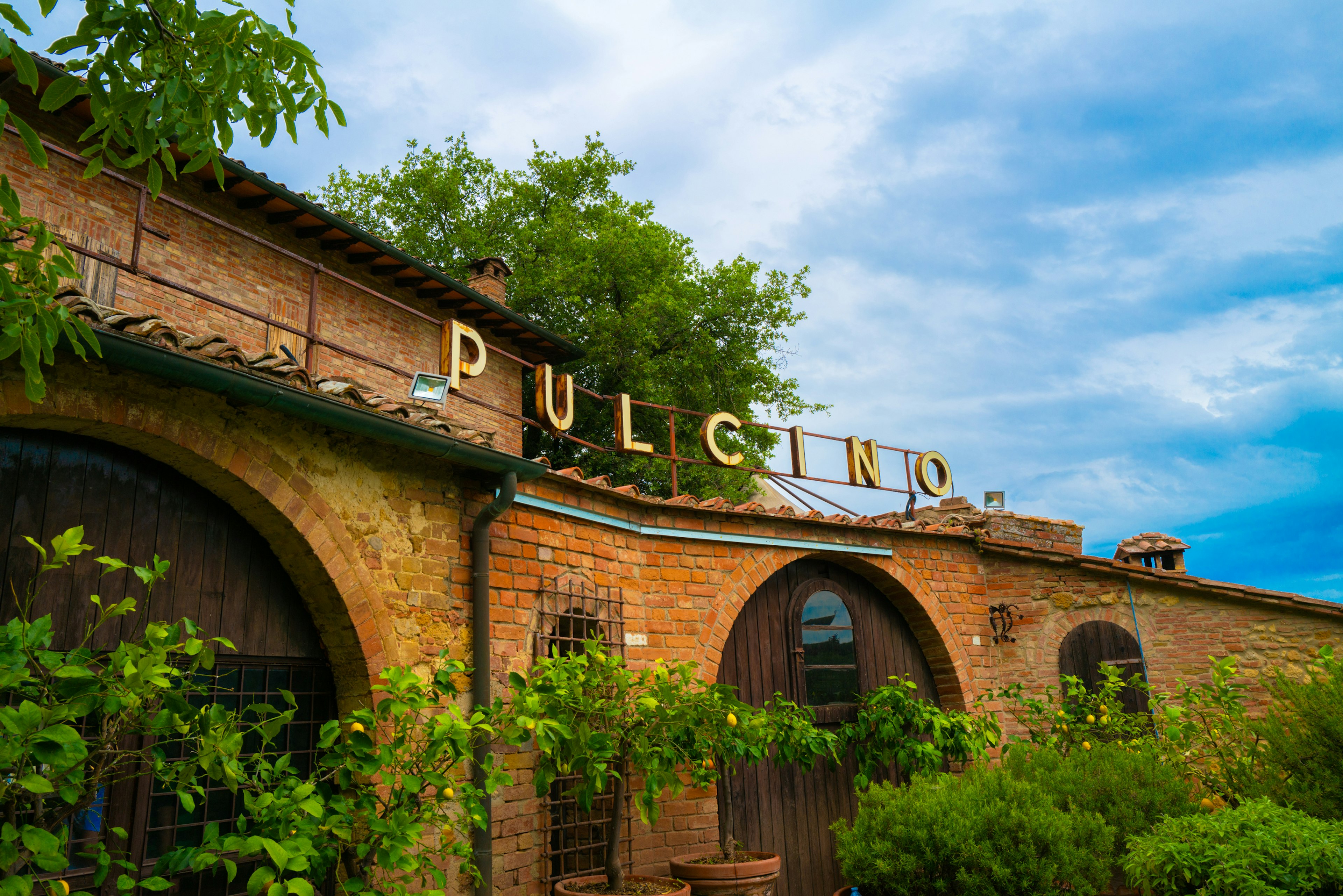 緑に囲まれた古いレンガの建物に「PULCINO」の看板がある