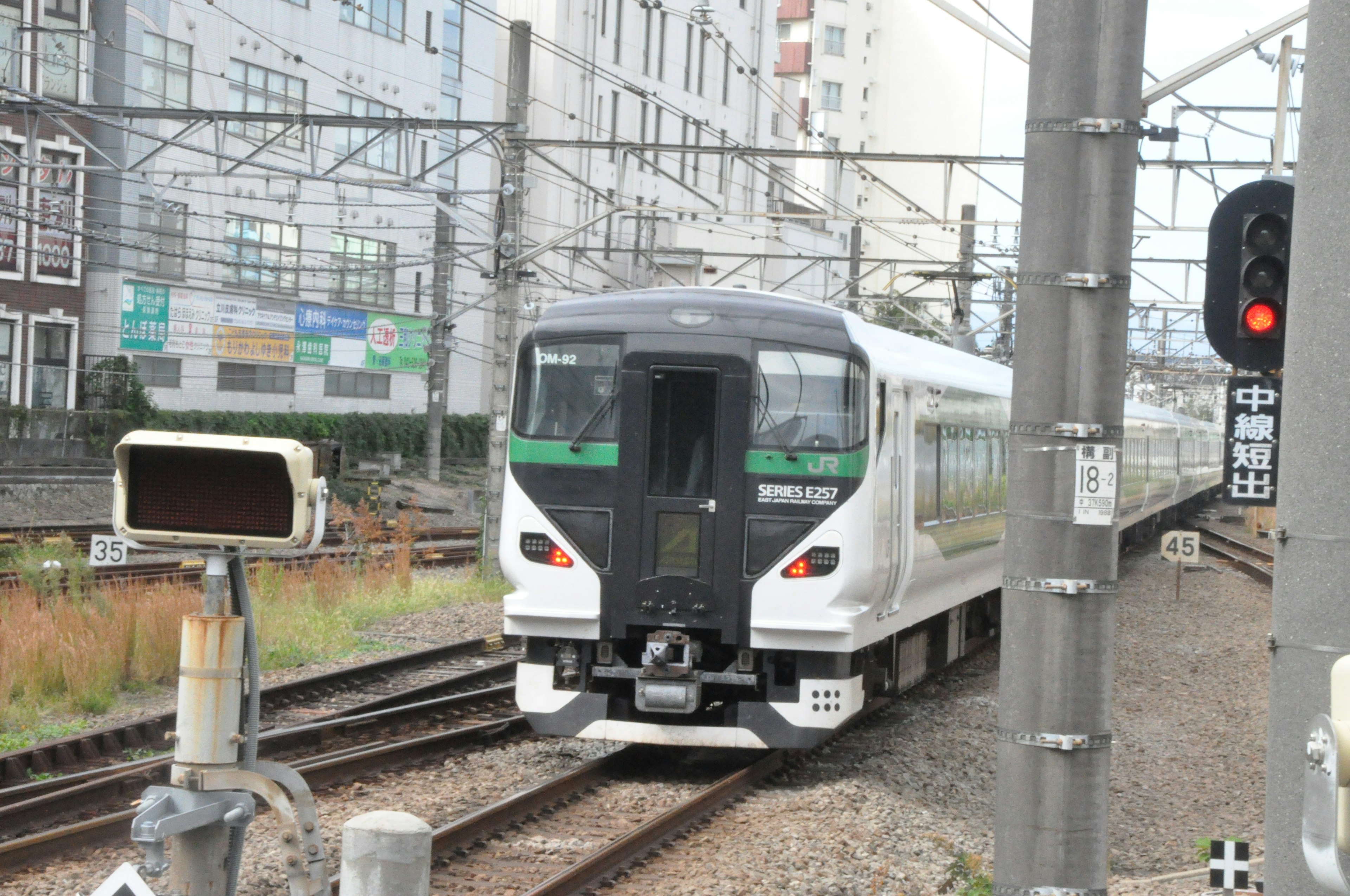 A white train approaching on the tracks with a railway signal and surveillance camera visible