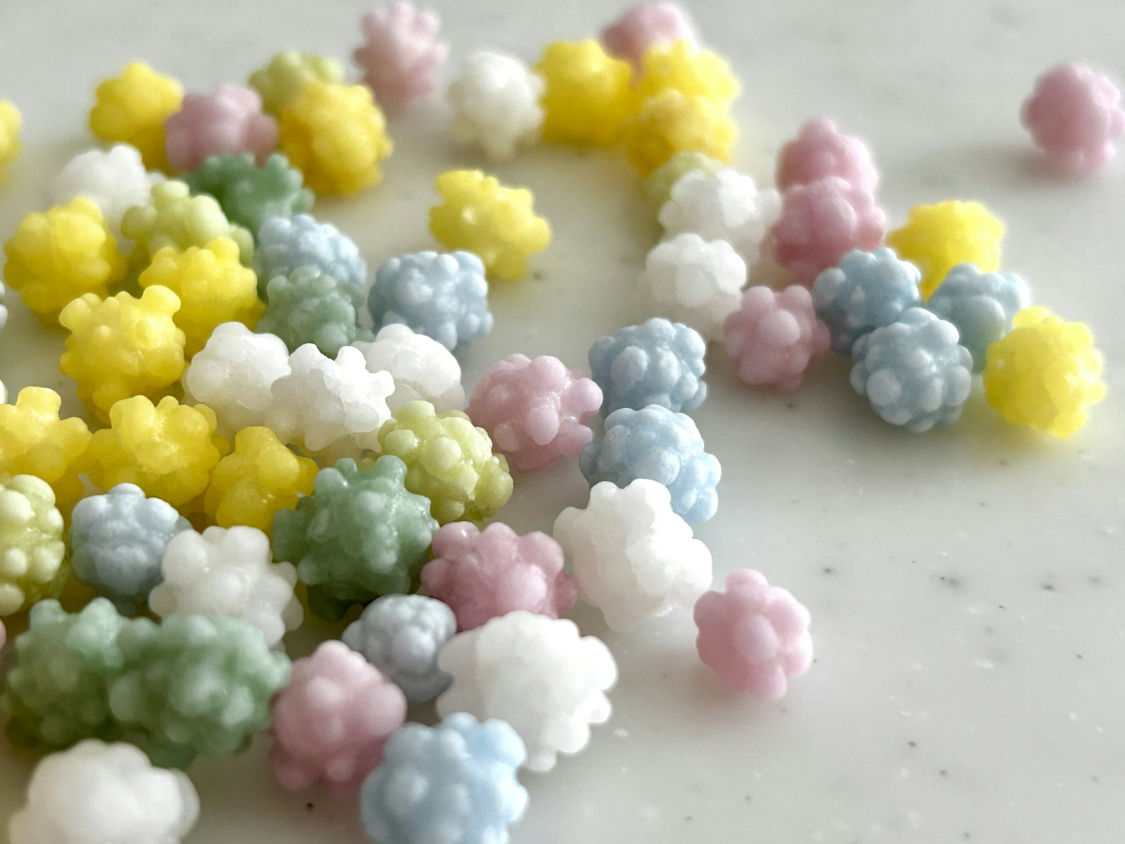 Caramelle colorate a forma di piccoli fiori sparse su uno sfondo bianco