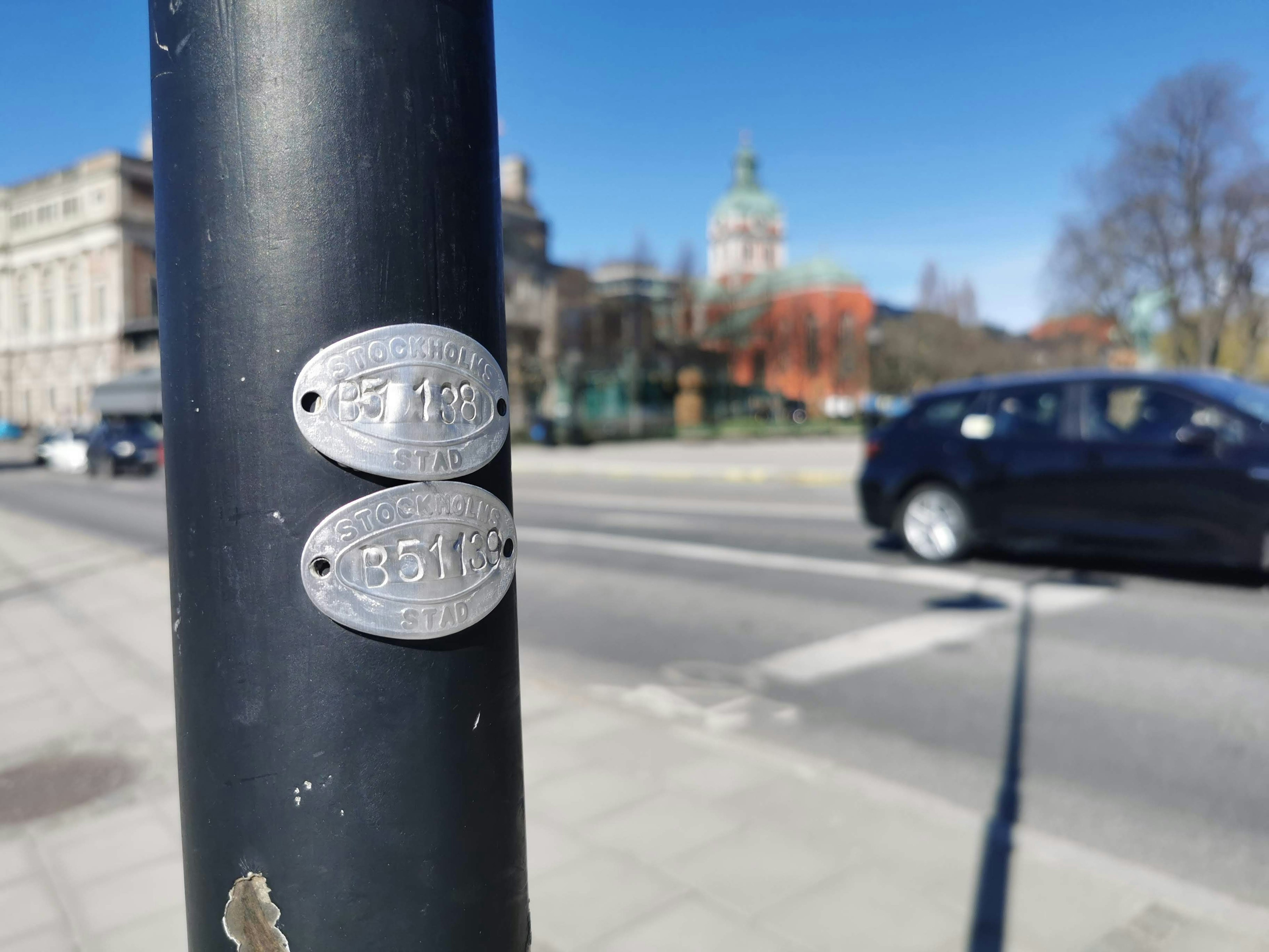 Zwei Metallplatten, die an einem schwarzen Pfosten in einer städtischen Umgebung befestigt sind