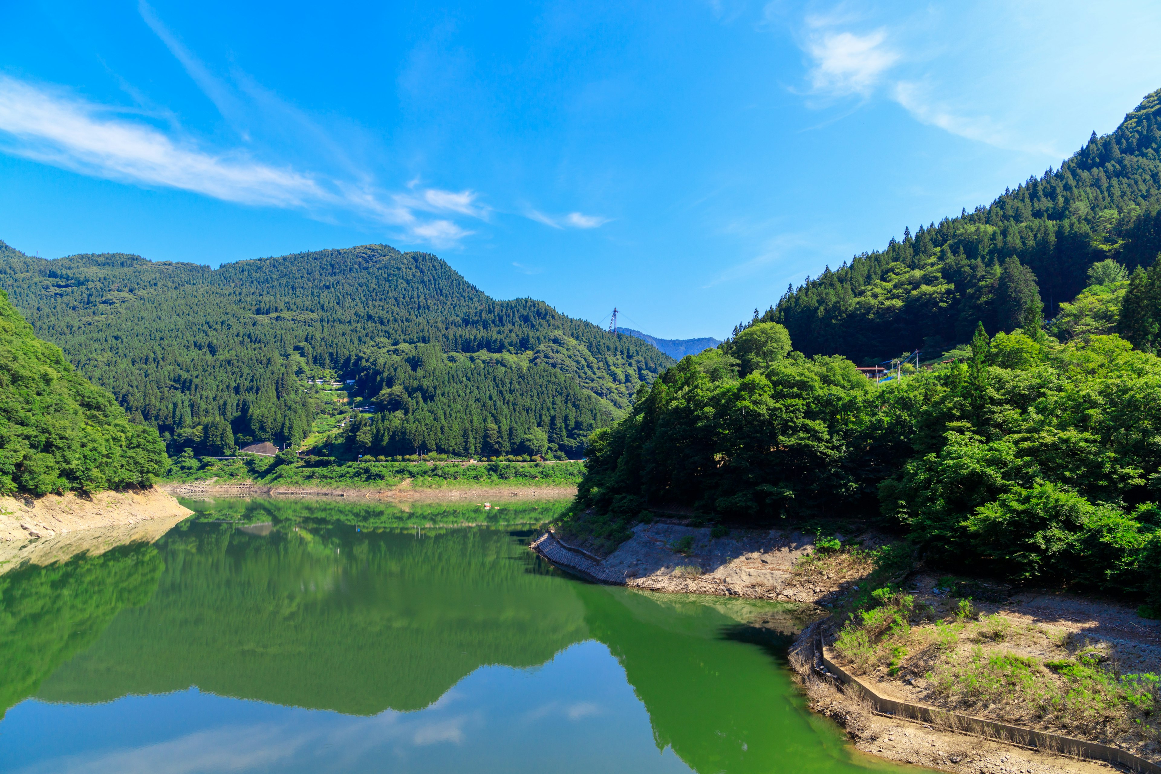 Danau tenang yang mencerminkan langit biru dan gunung hijau