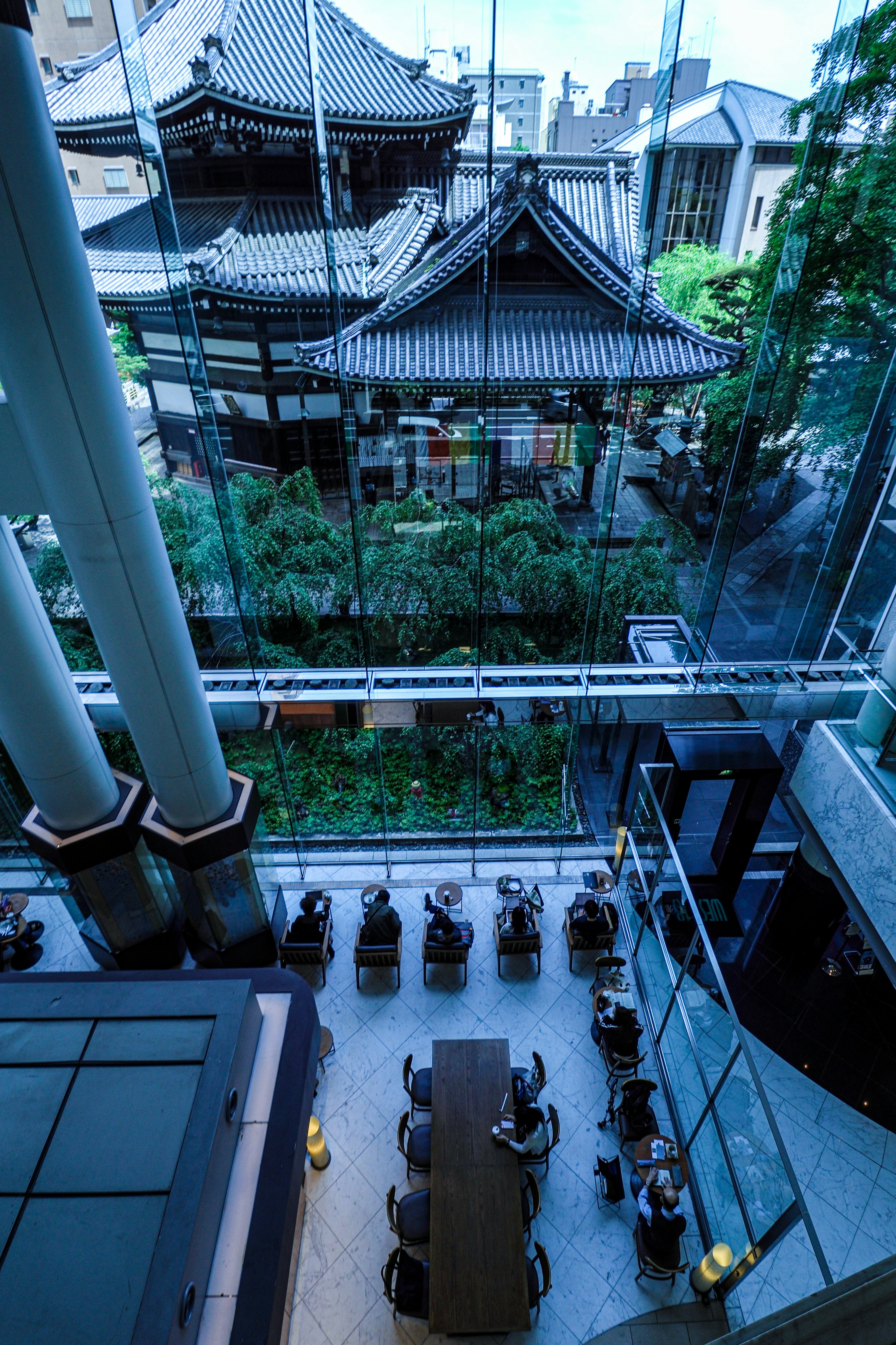 Modern glass building featuring a traditional Japanese structure and lush greenery in the courtyard