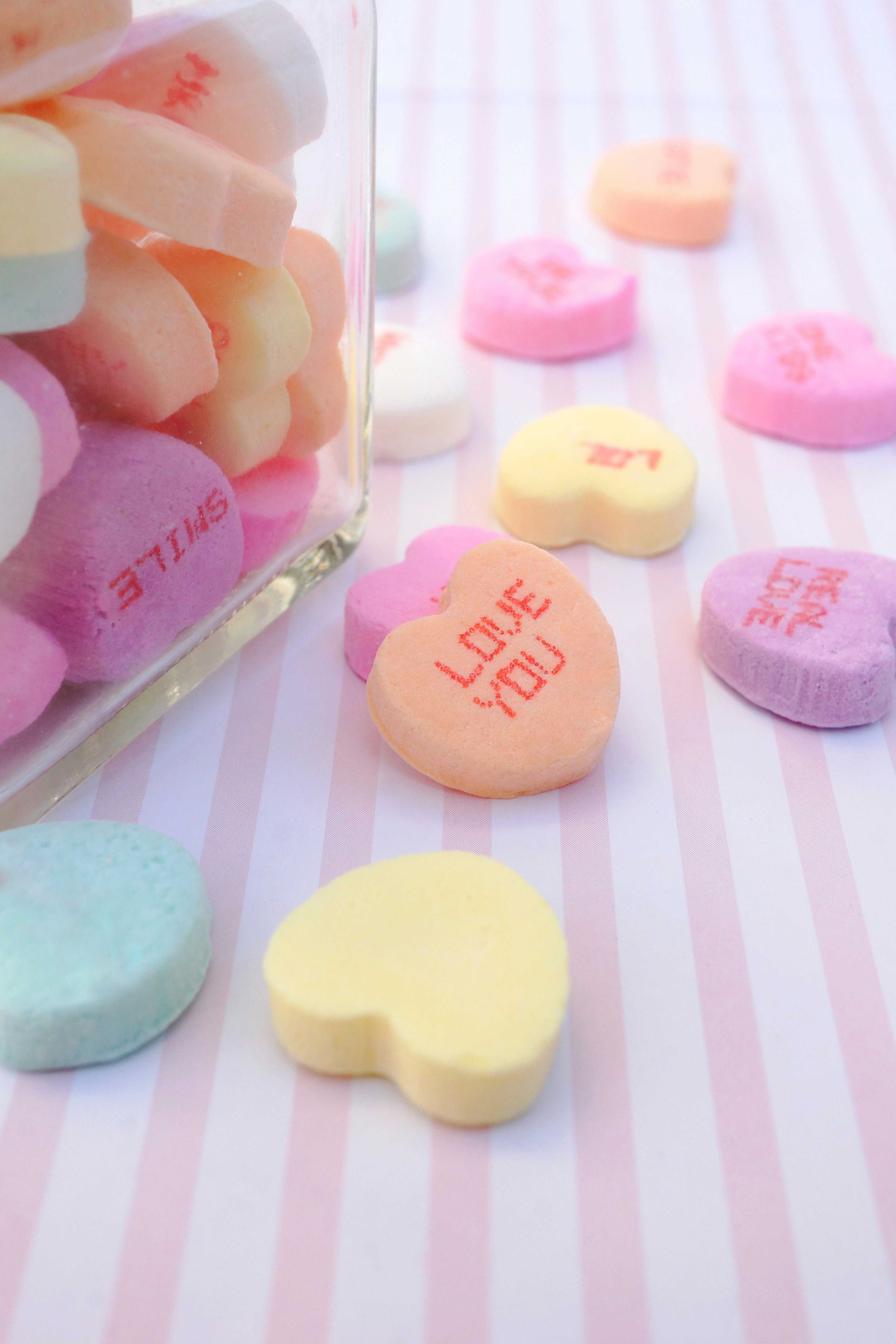 Colorful heart-shaped candies spilling out of a glass jar