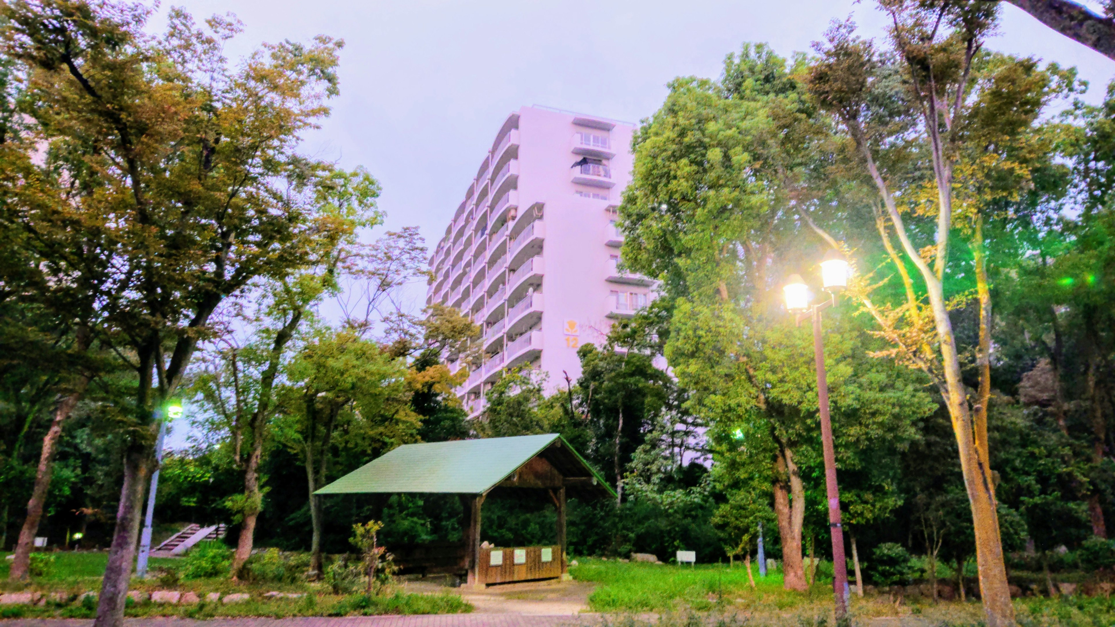 公園の緑に囲まれたピンクの建物と小屋の景観