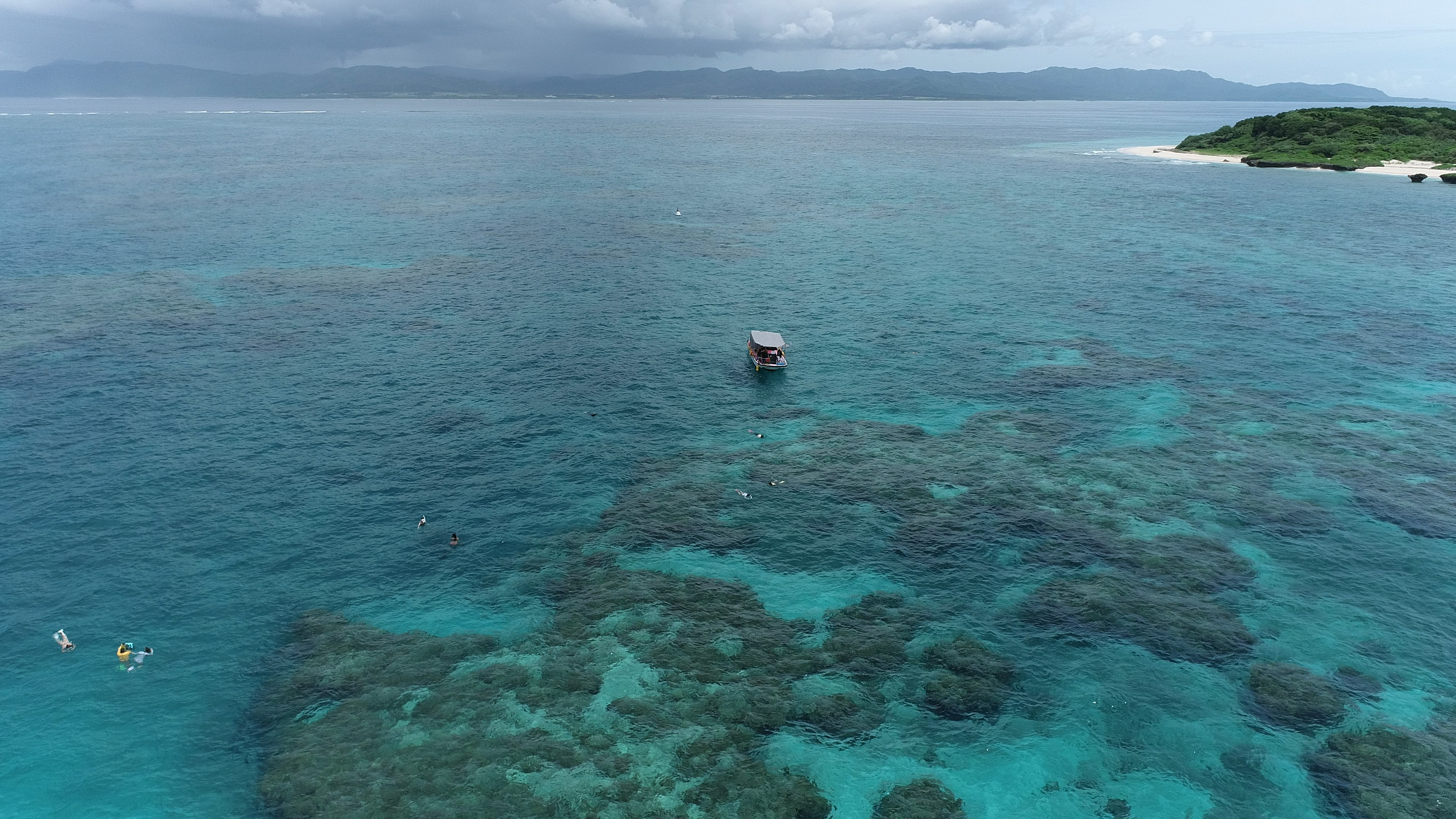 Un bateau flottant au-dessus des récifs coralliens dans une mer turquoise avec des nageurs à proximité