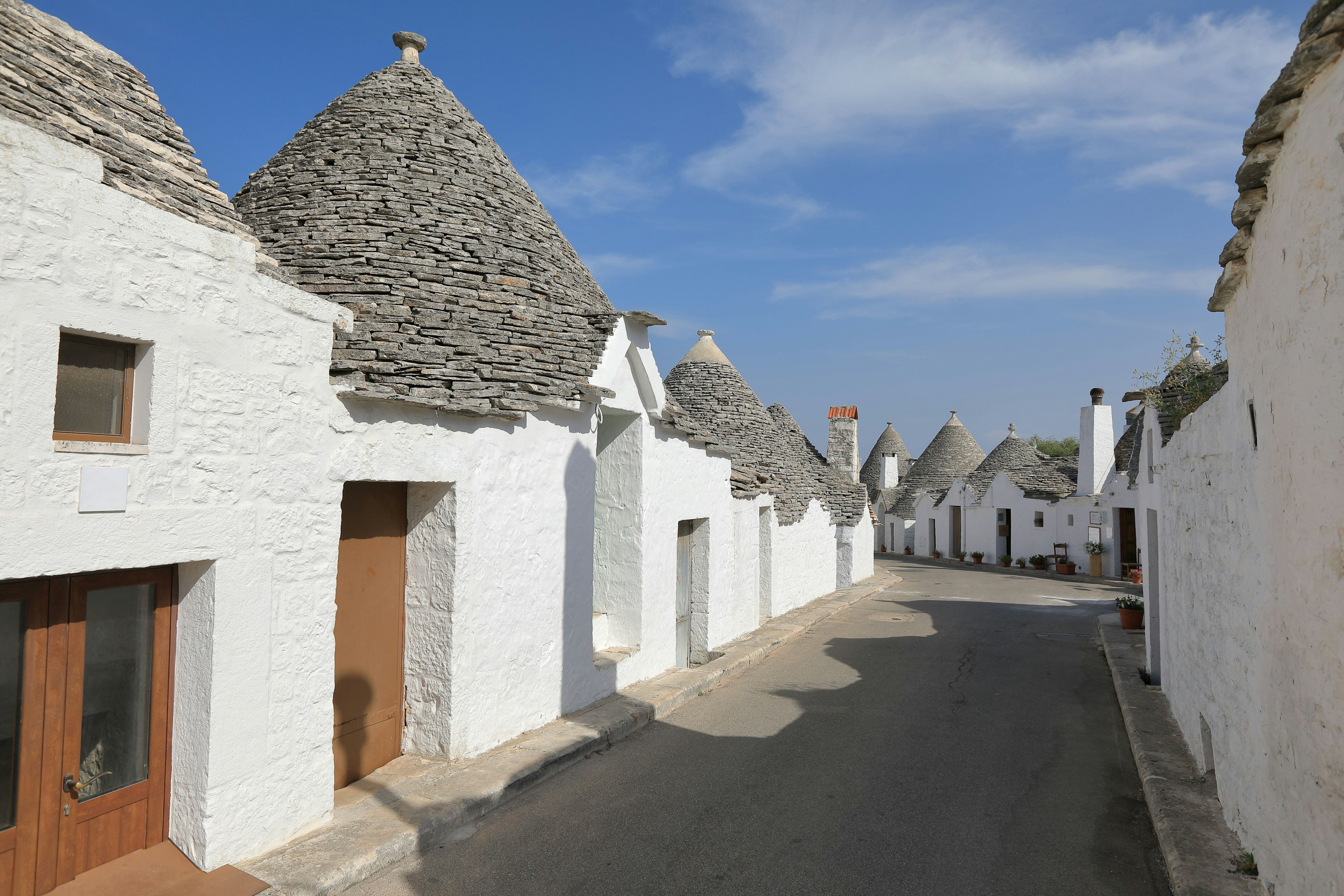 Strada tranquilla fiancheggiata da case trulli bianche con tetti in pietra grigia