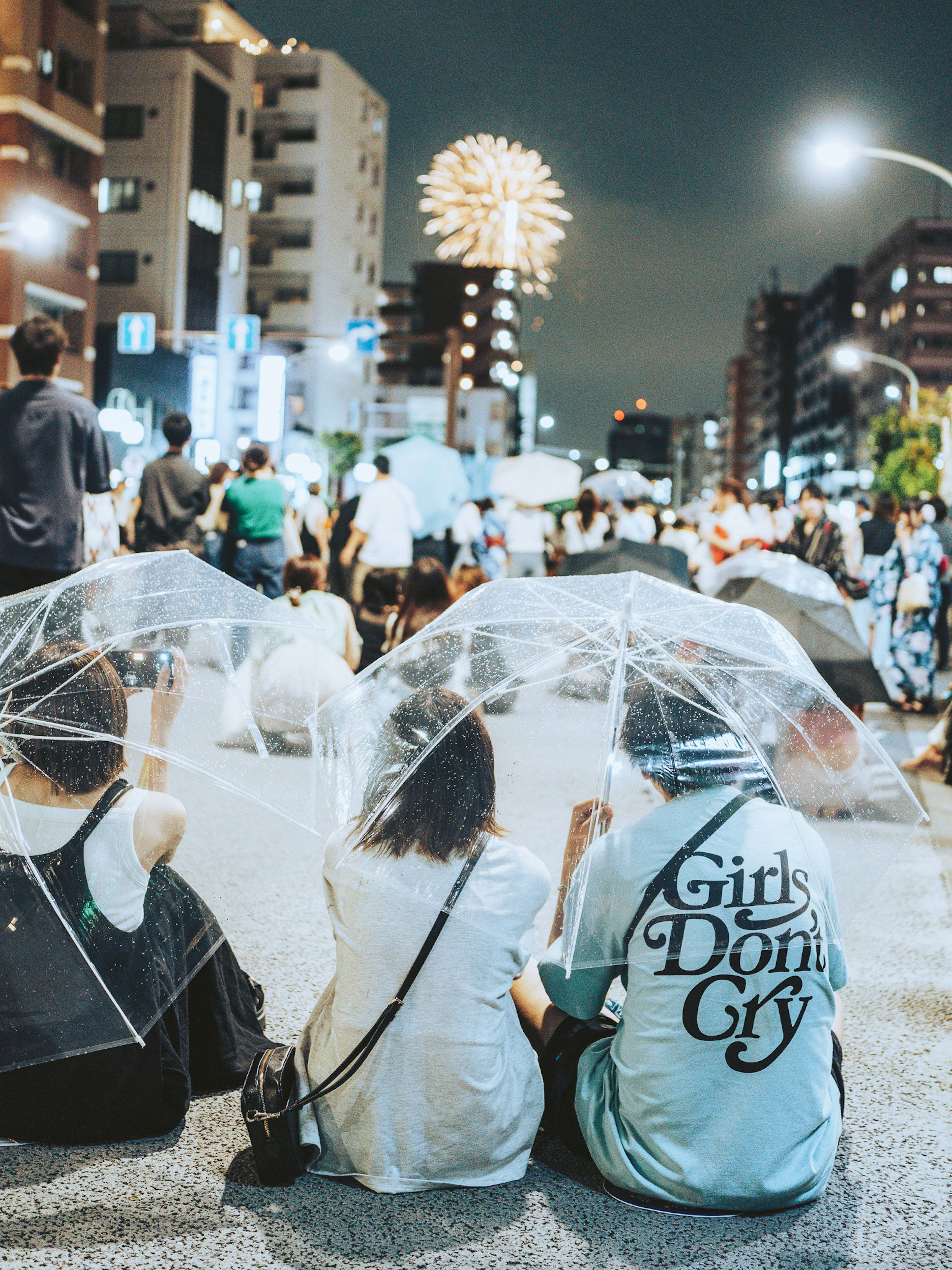 夜の祭りを楽しむ人々と花火を背景にした透明な傘を持つ若者たち