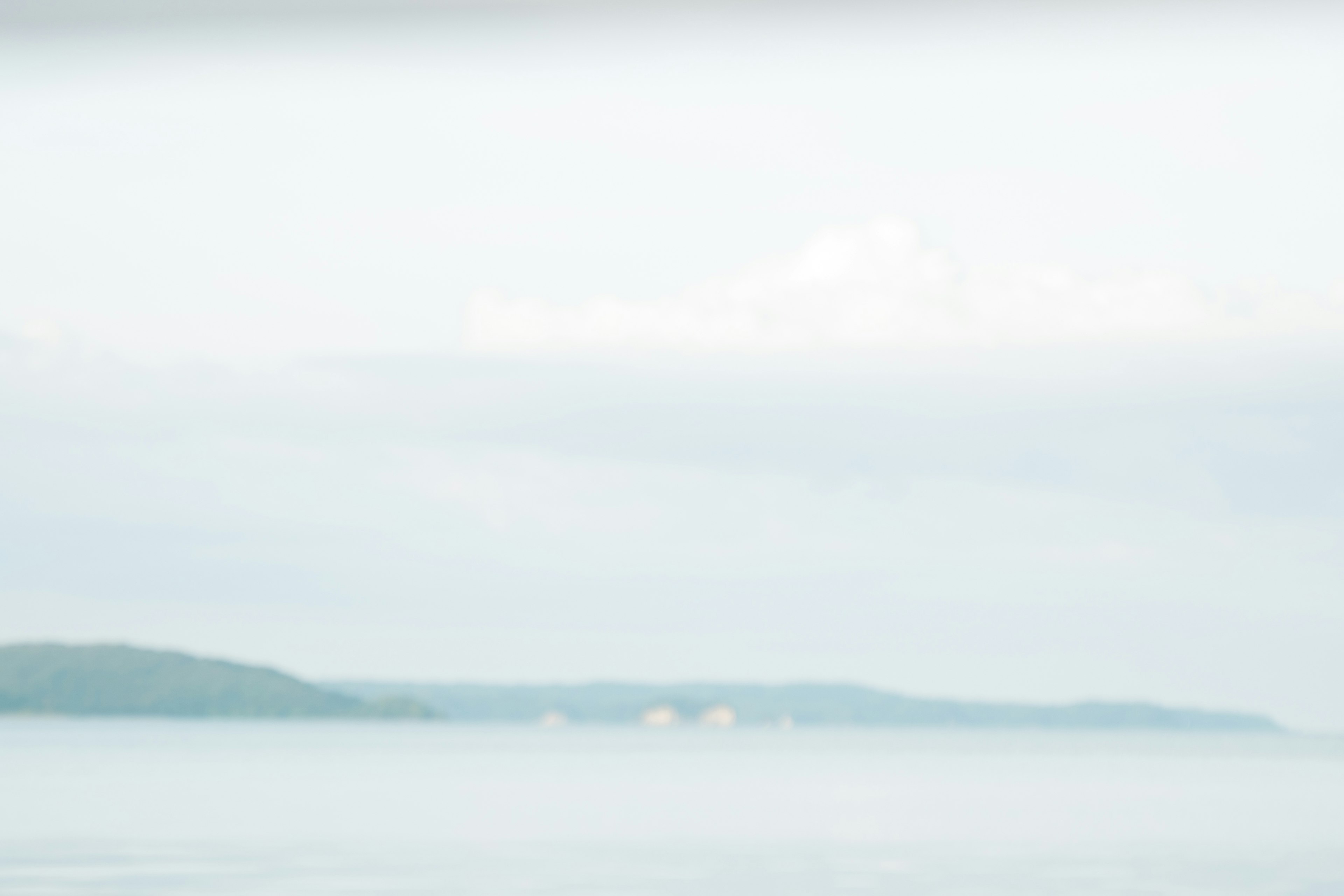 Calm sea landscape with soft blue and white tones featuring distant islands