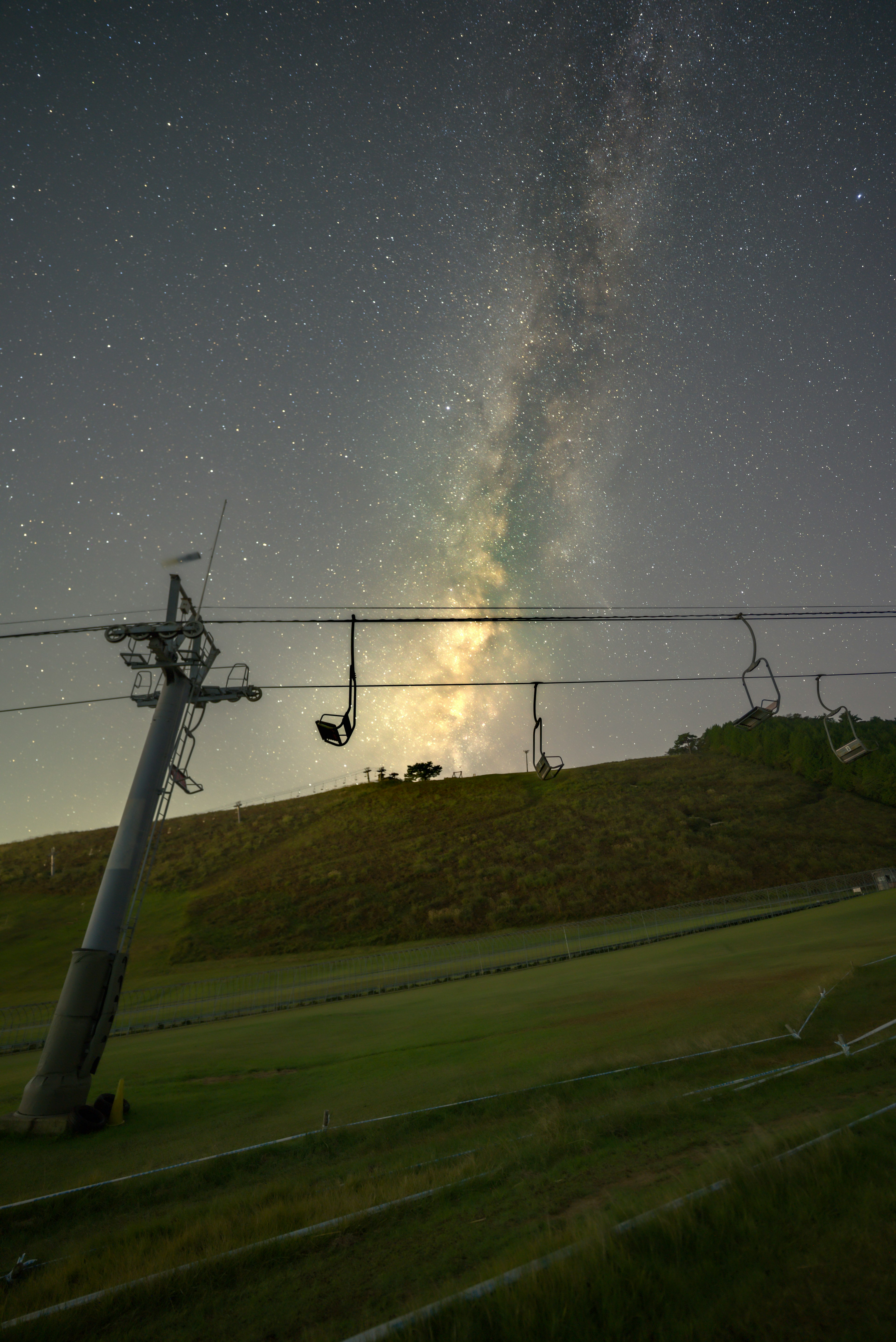 Night scene with a ski lift and green hills under a starry sky