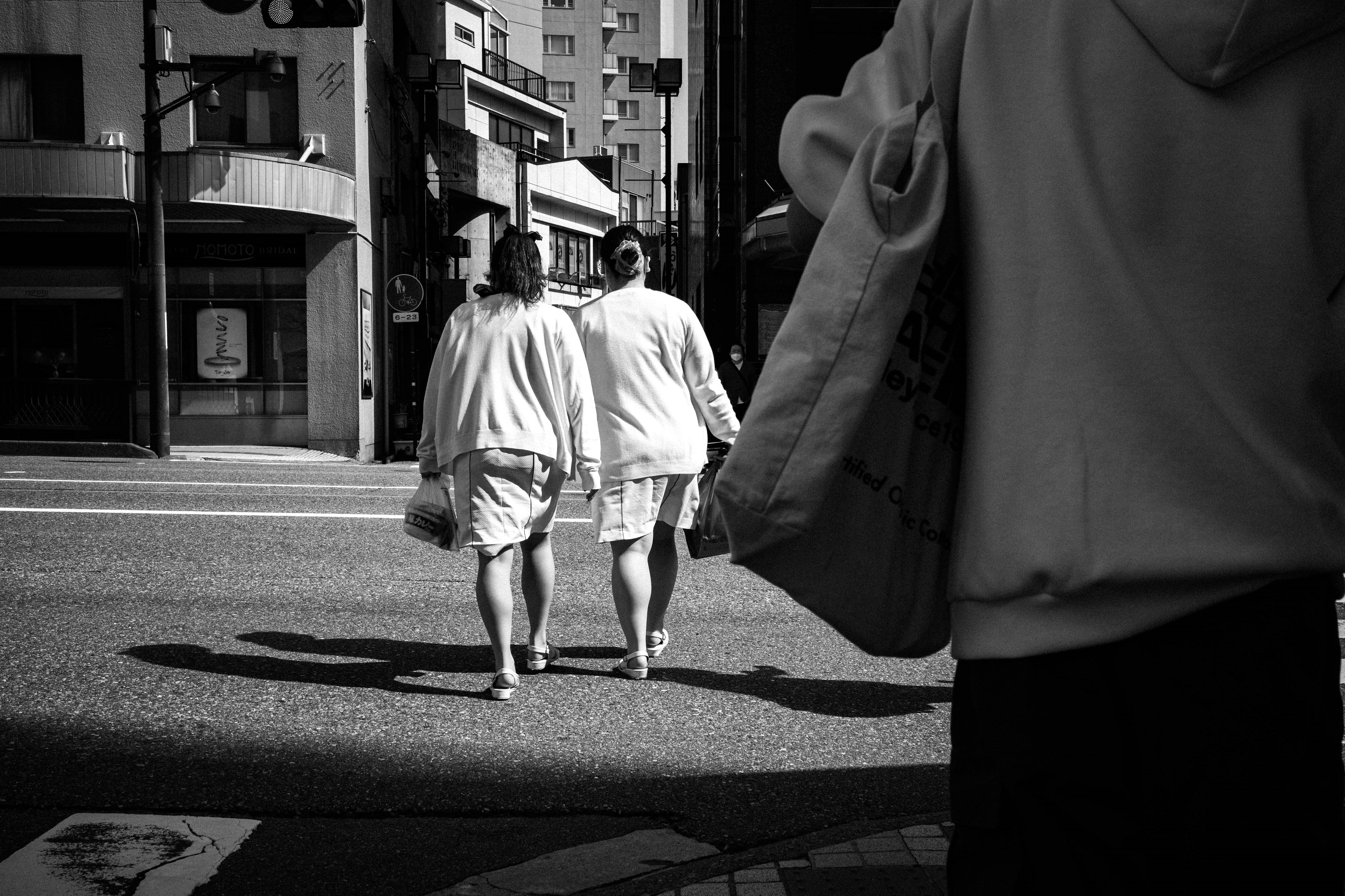 Dos figuras caminando en una escena de calle en blanco y negro con una bolsa en primer plano